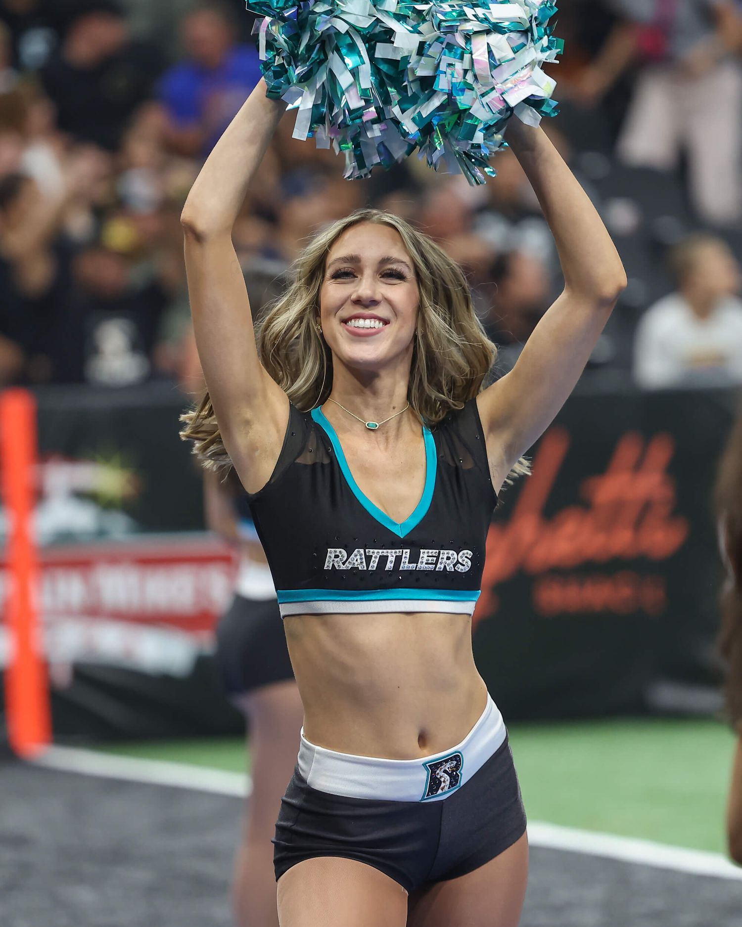 Rattlers cheerleader performs with pom poms at indoor arena football game.