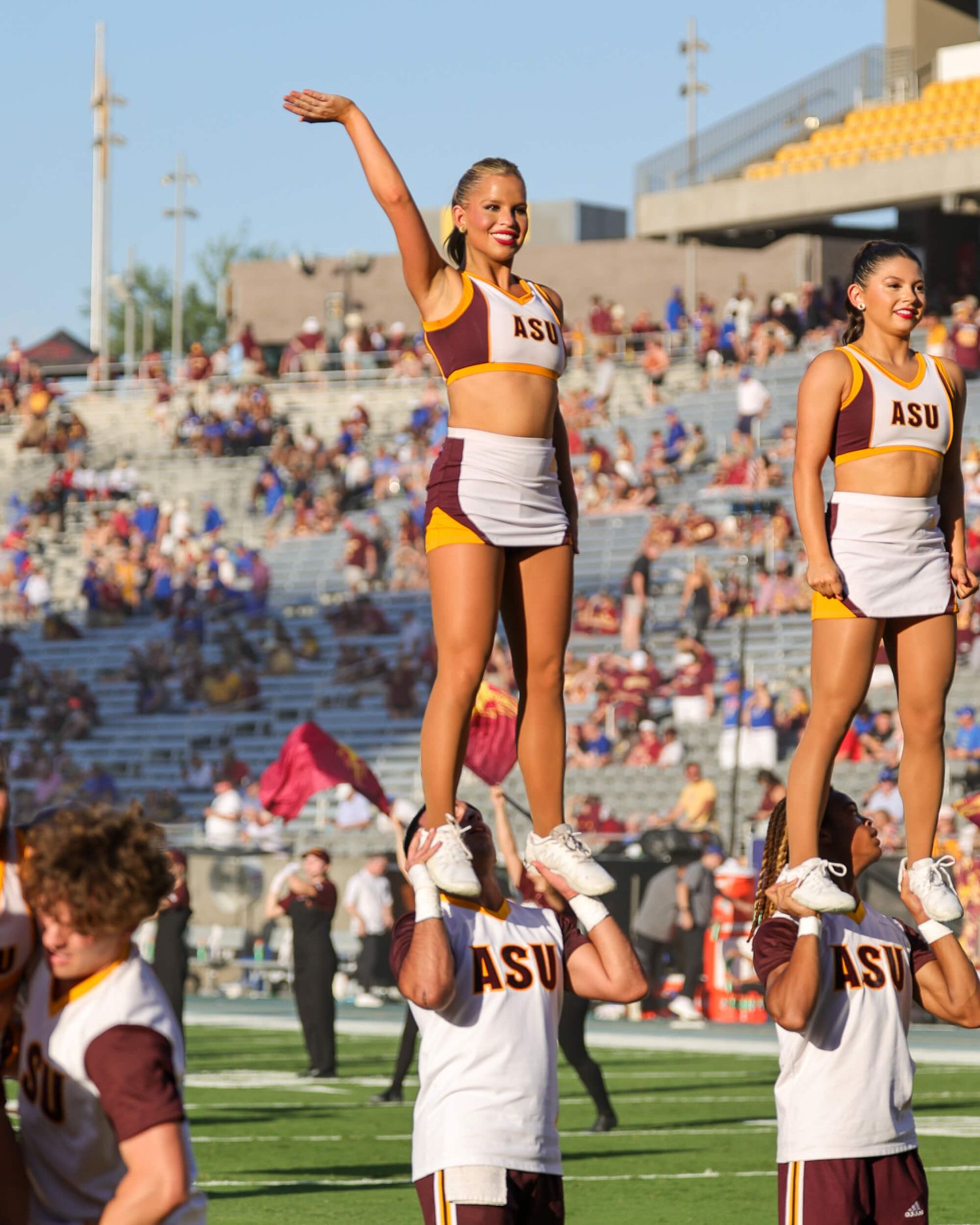 ASU cheerleaders perform a stunt at a college football game, with one cheerleader elevated above the crowd.