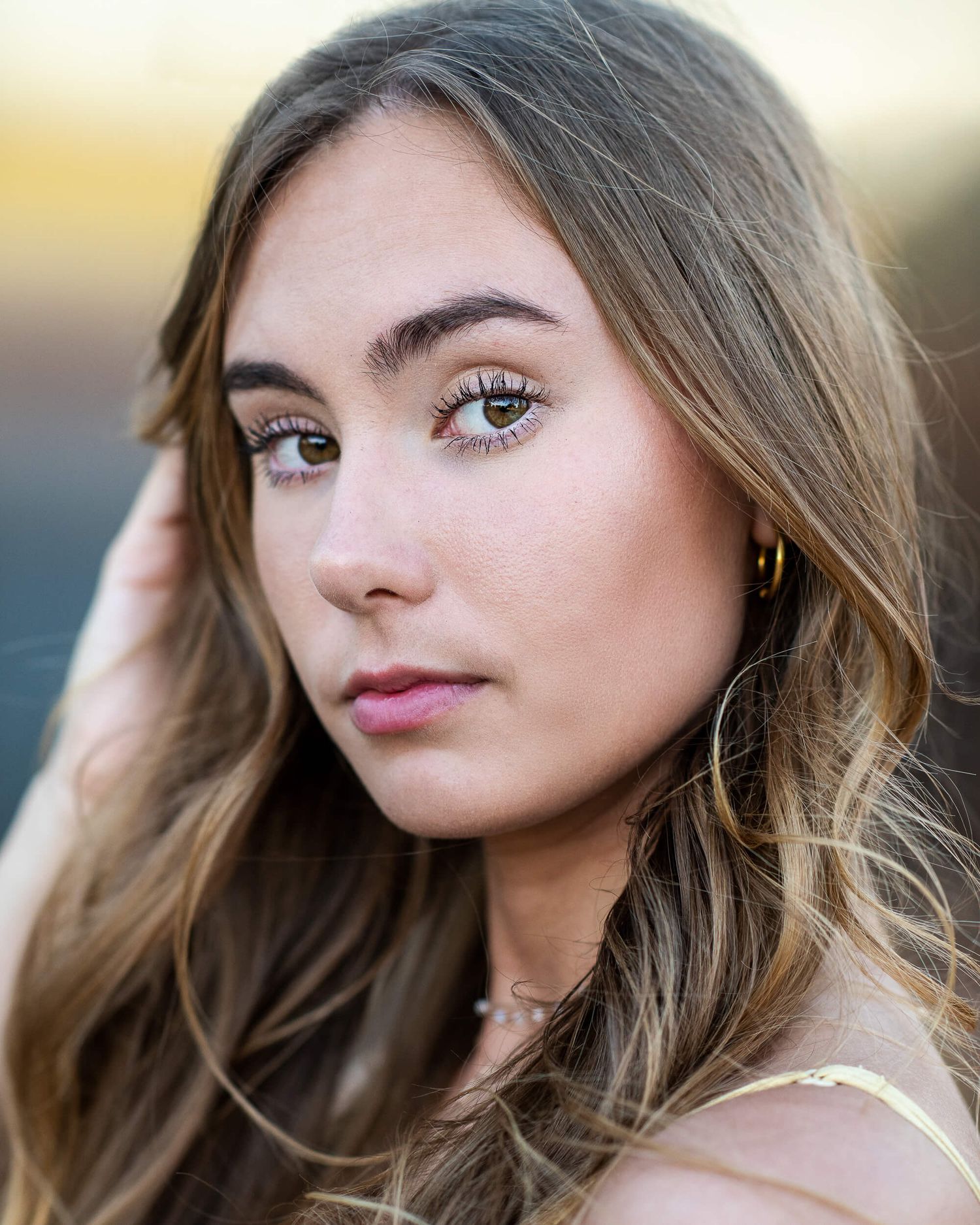 Young brunette woman with wavy hair and hoop earrings in natural light portrait.