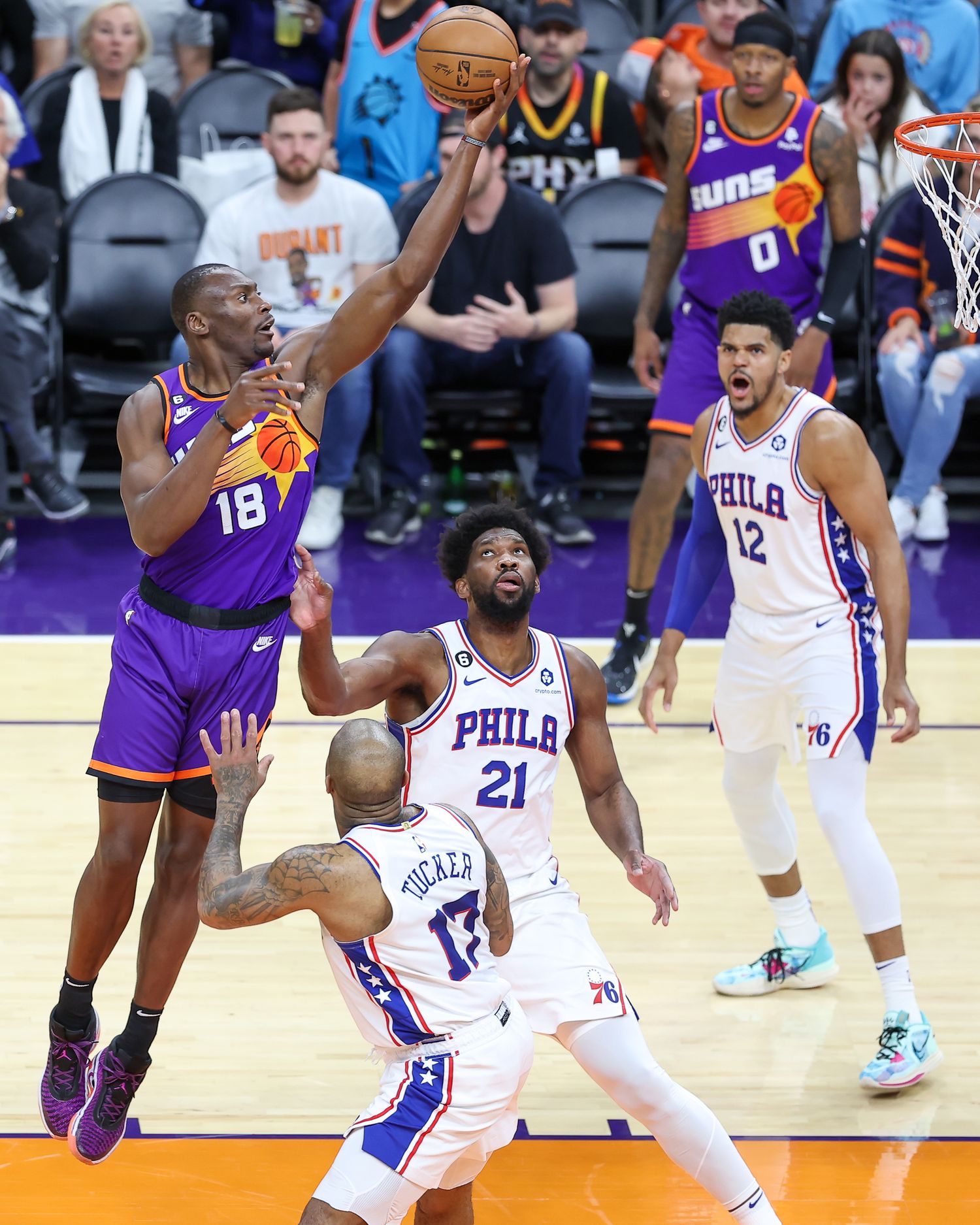 Phoenix Suns player number 18 drives to basket against Philadelphia 76ers defenders during NBA game.