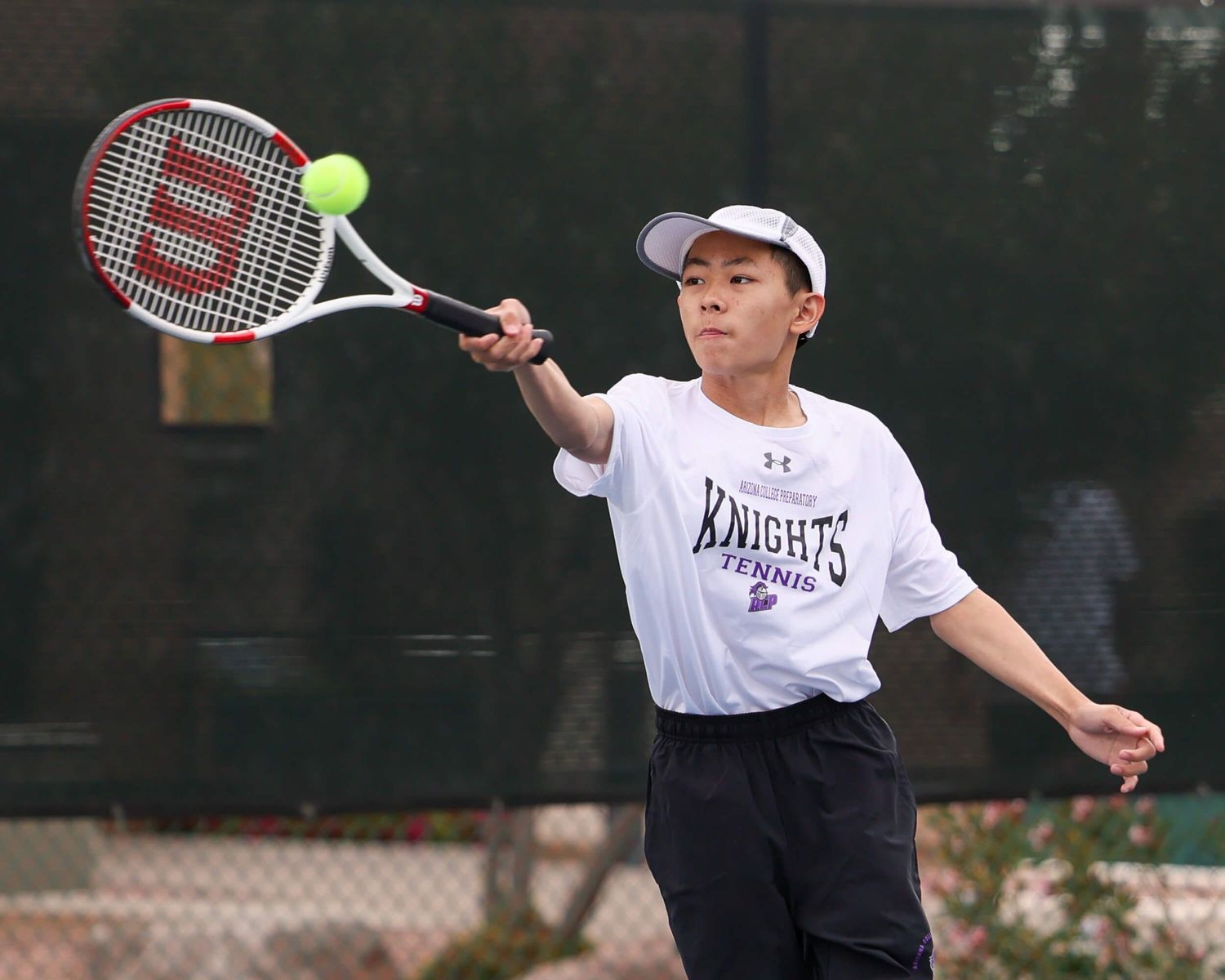 Young male tennis player in Knights uniform hits a forehand shot during a match.