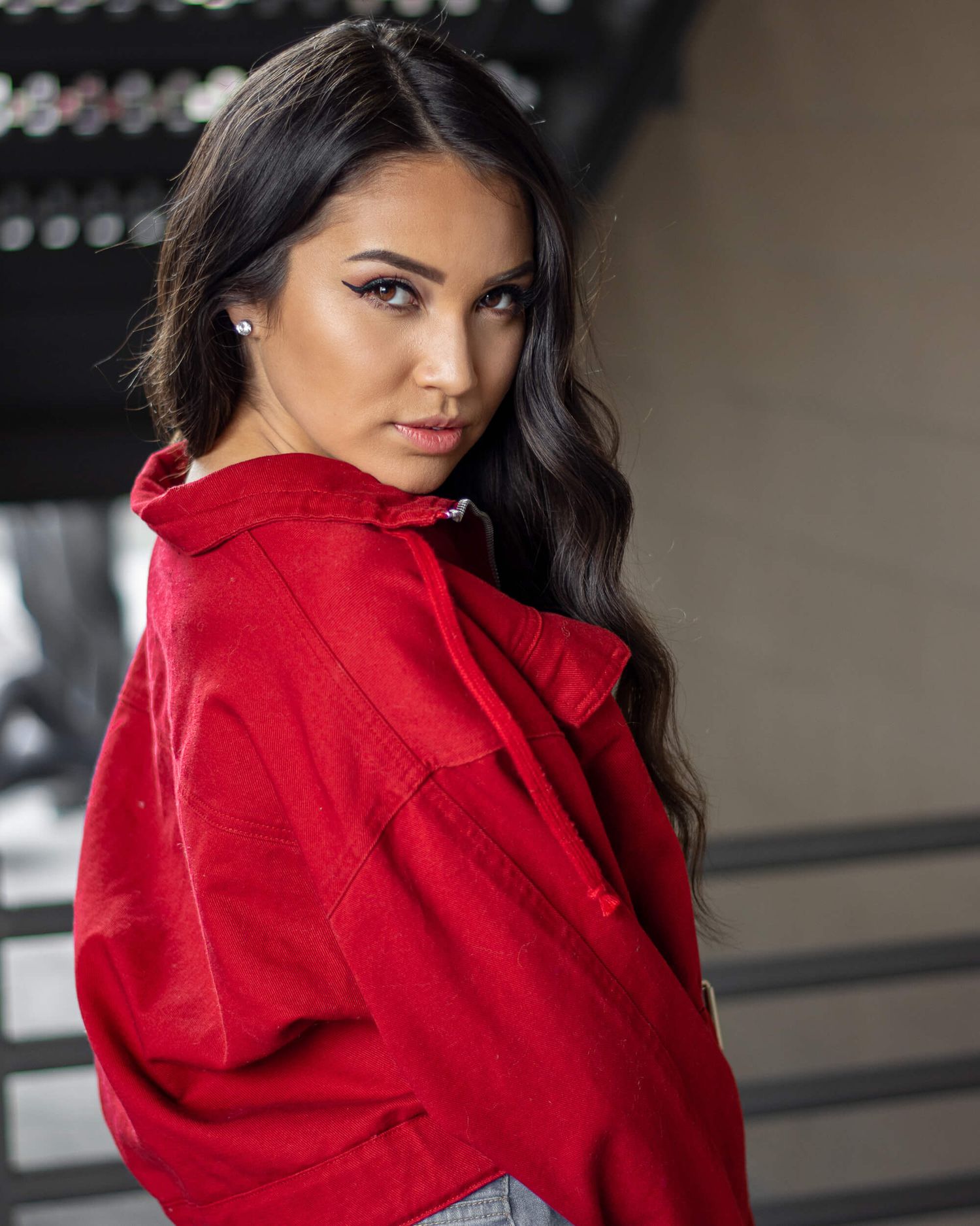 Woman in red shirt glancing over shoulder in urban setting.