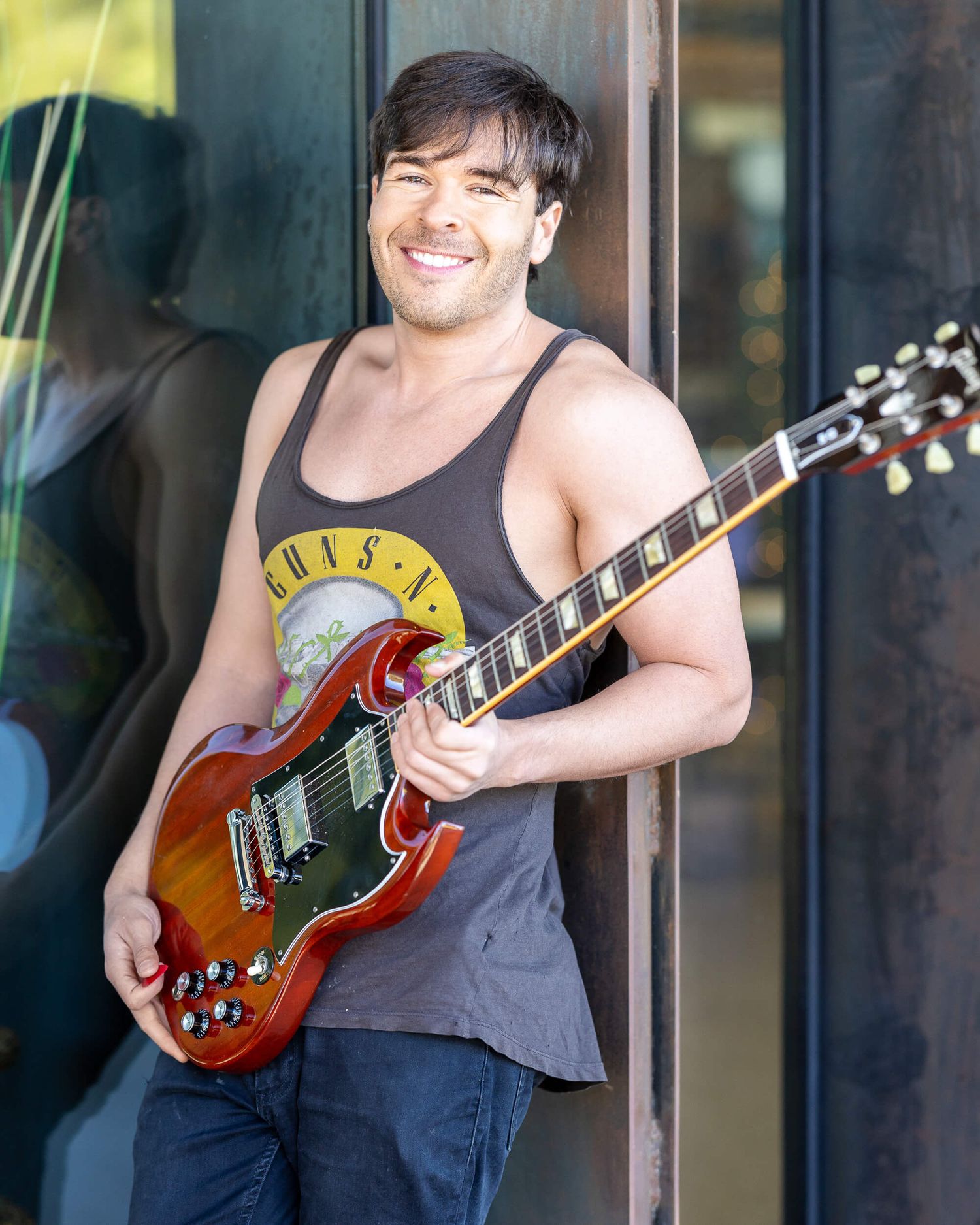 Smiling man in tank top playing electric guitar outdoors.