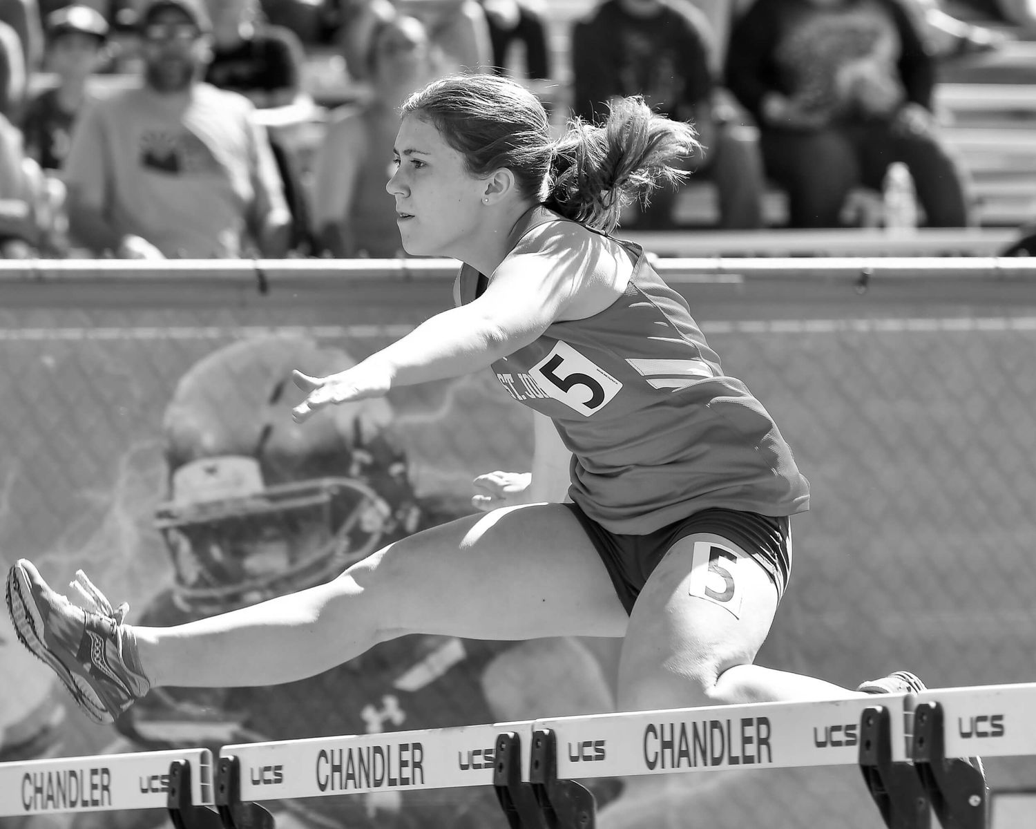 Female athlete clears hurdle during track and field competition at Chandler stadium.