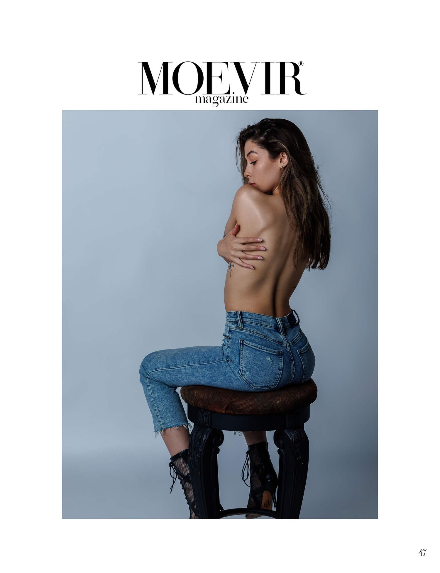 Woman poses topless in high-waist jeans on stool for Moevir Magazine fashion editorial.