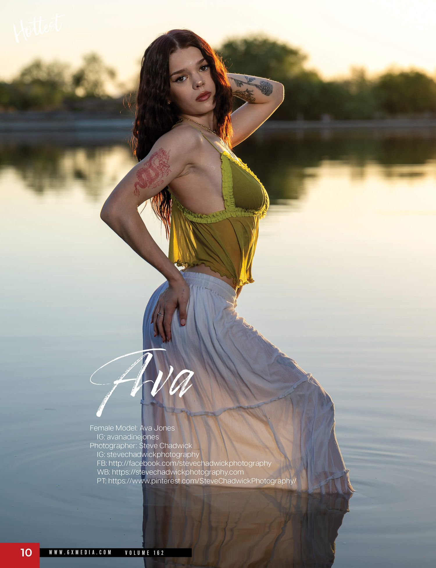 A brunette model poses in a sheer yellow top and white skirt standing in shallow water at golden hour.