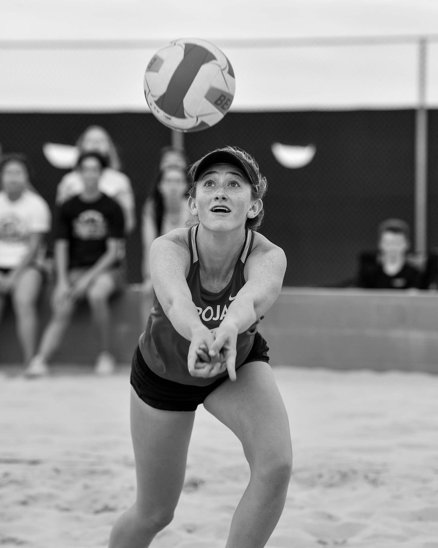 Female beach volleyball player bumps the ball in a black and white action sports photograph.