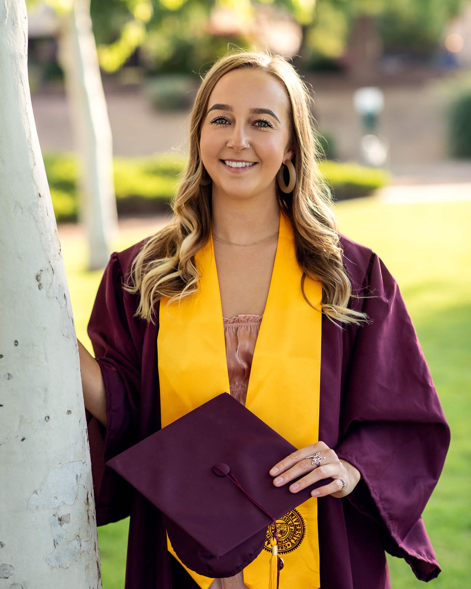 Smiling blonde woman in maroon graduation gown holding cap with gold ASU stole.