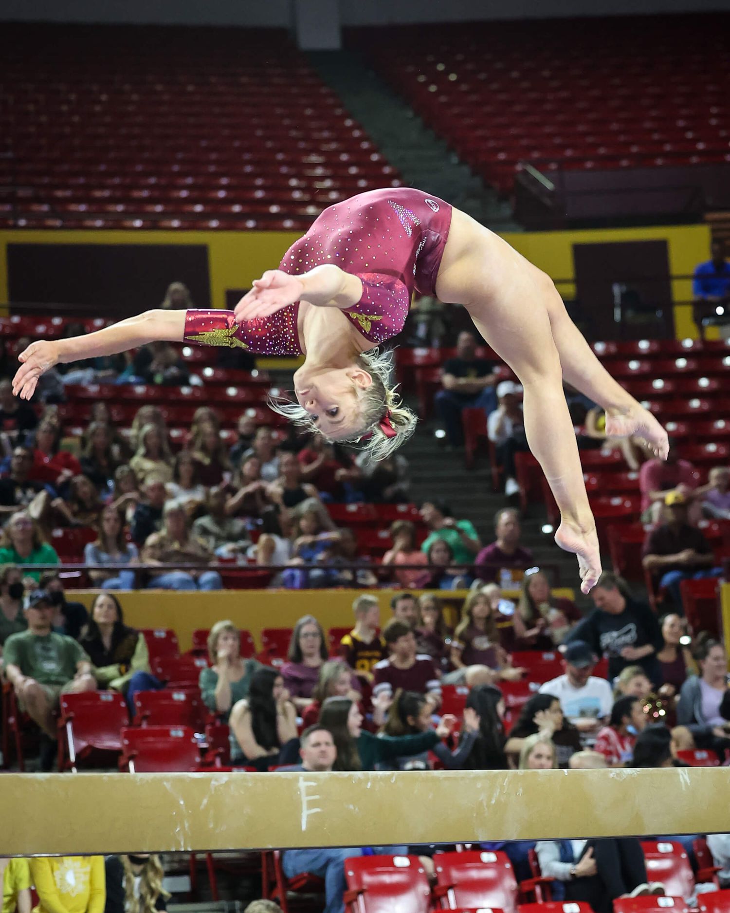 ASU gymnast performs a back walkover on the balance beam in a sparkly maroon leotard during competition.