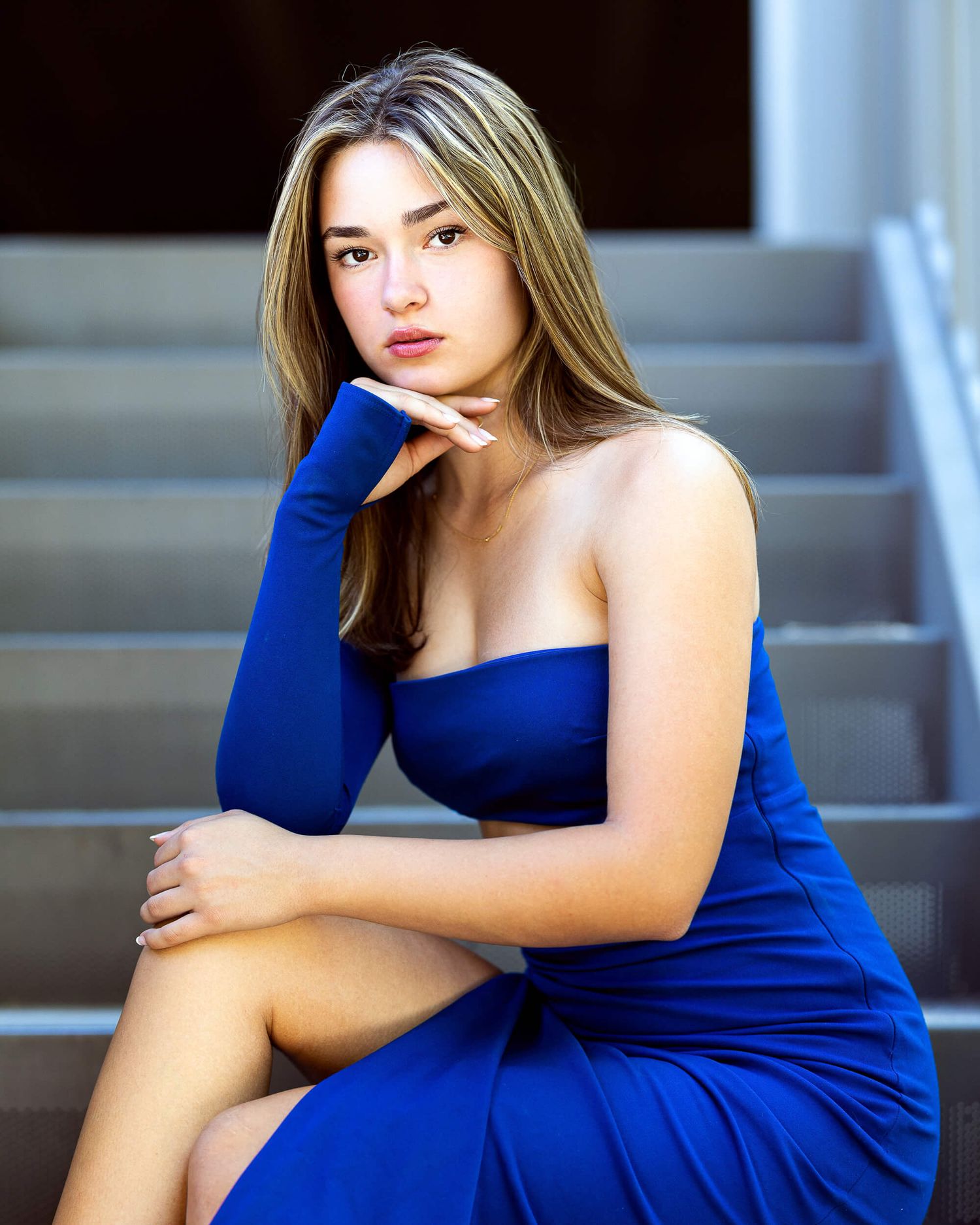 Young woman in a royal blue strapless dress and glove sits on steps in an elegant portrait pose.