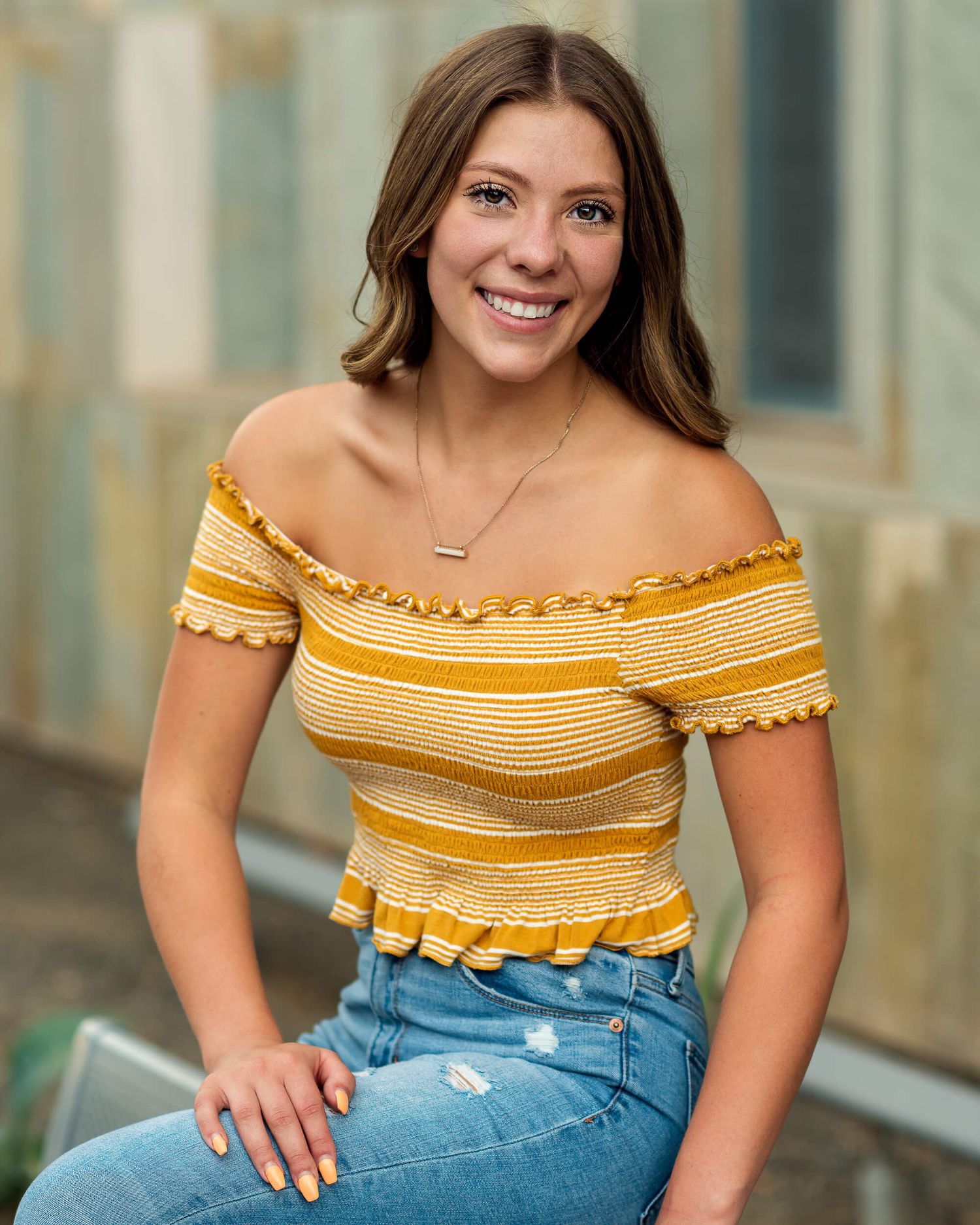 Smiling young woman in yellow striped off-shoulder top and jeans senior portrait.