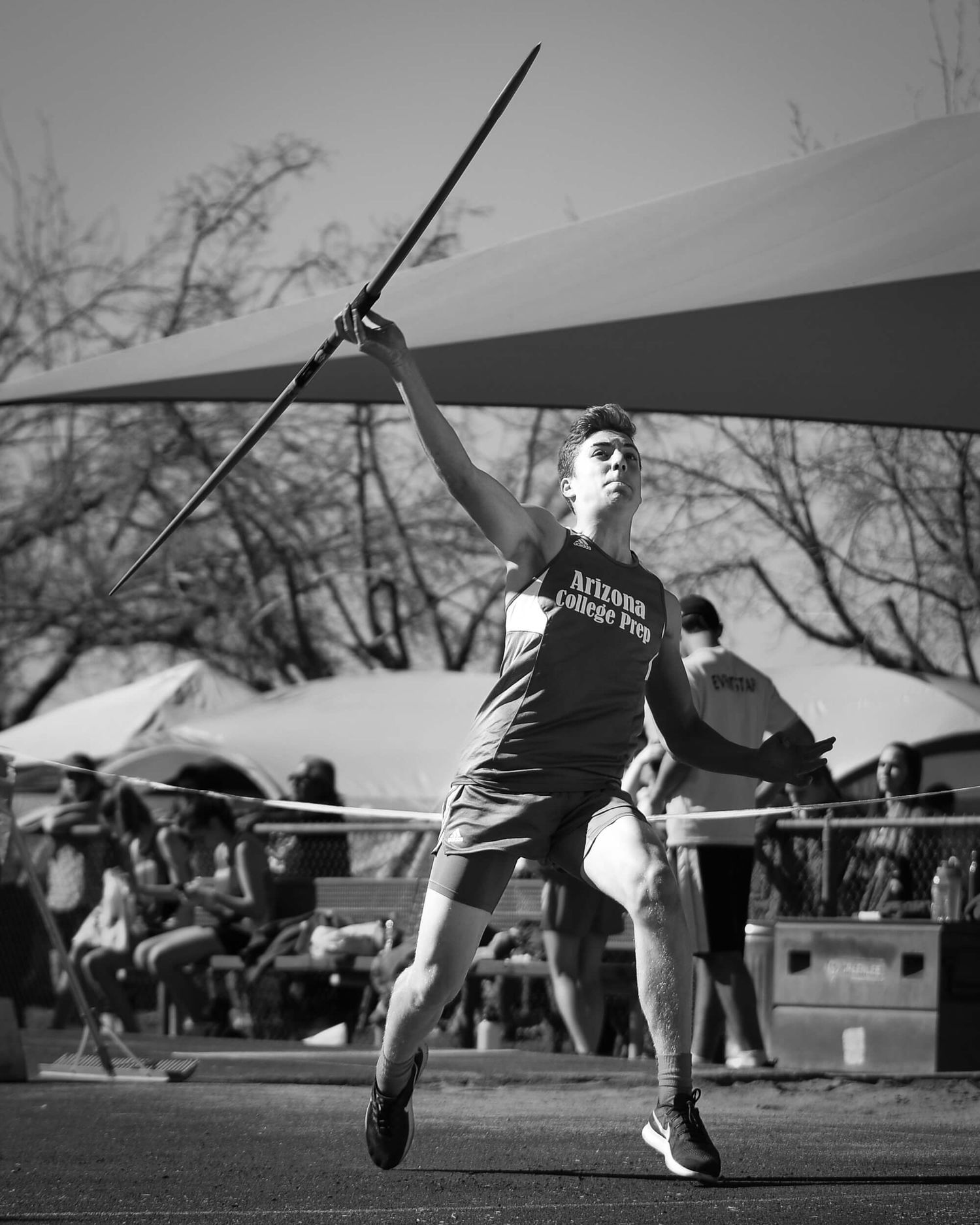 A male athlete prepares to throw a javelin during a black and white track and field event.