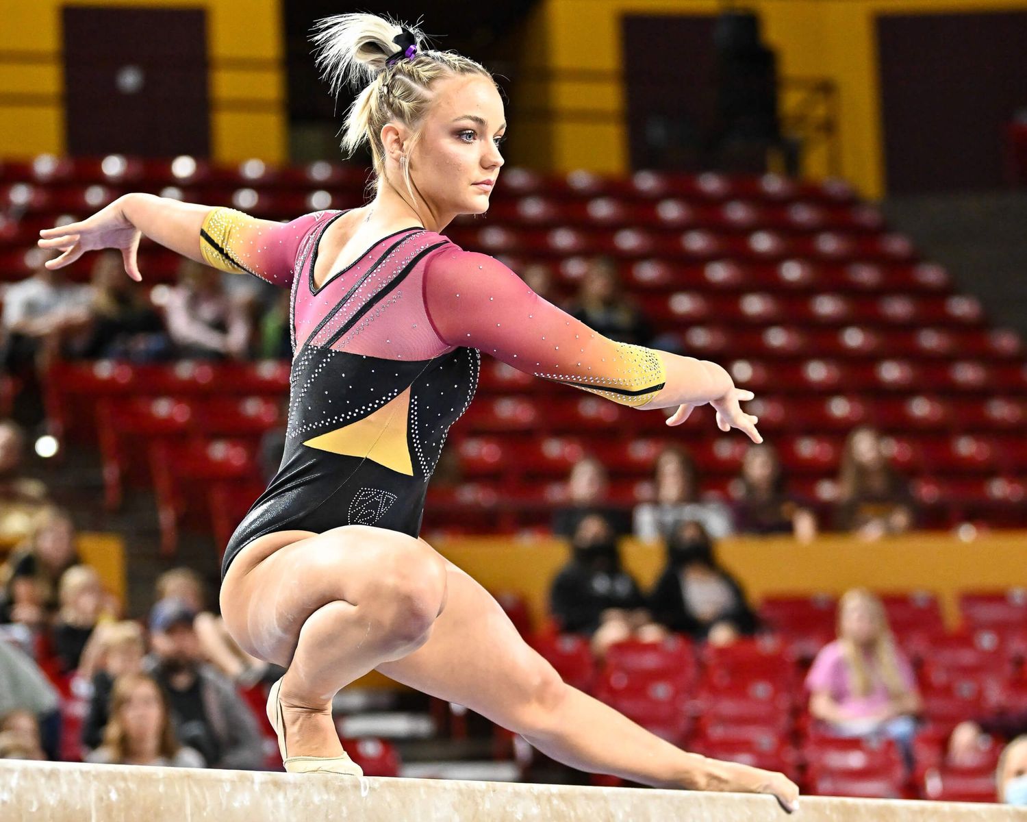 ASU gymnast in maroon and gold leotard performs a graceful pose on the balance beam during competition.