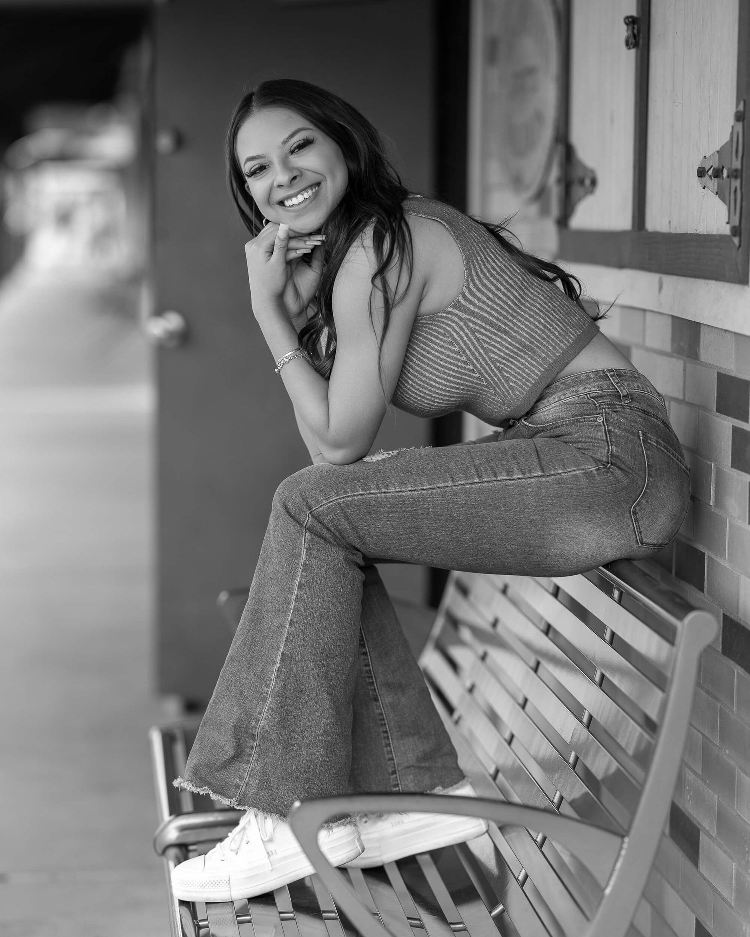 Black and white portrait of smiling young woman sitting on bench in casual jeans outfit.