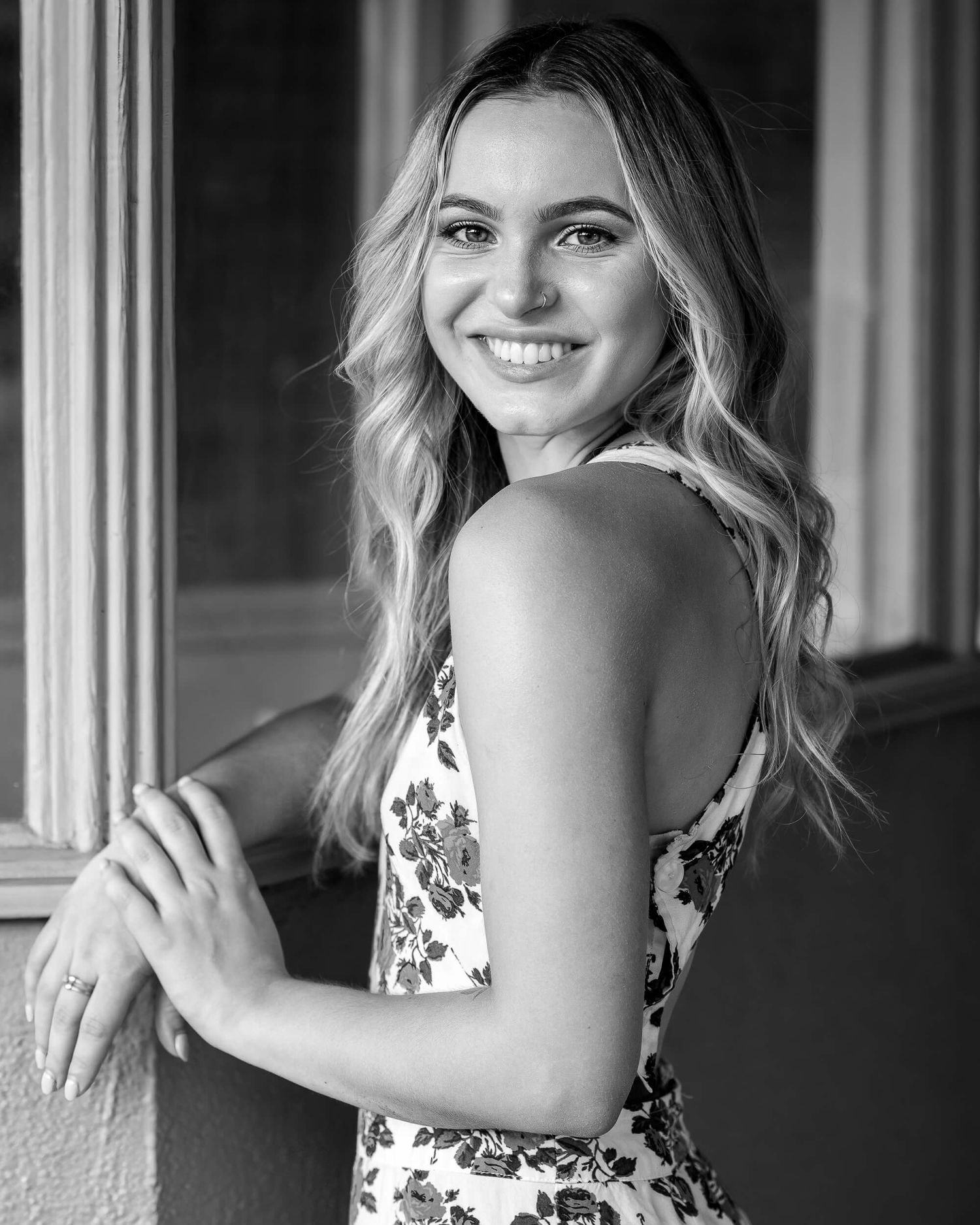 Smiling blonde woman in floral dress poses for black and white portrait photo.