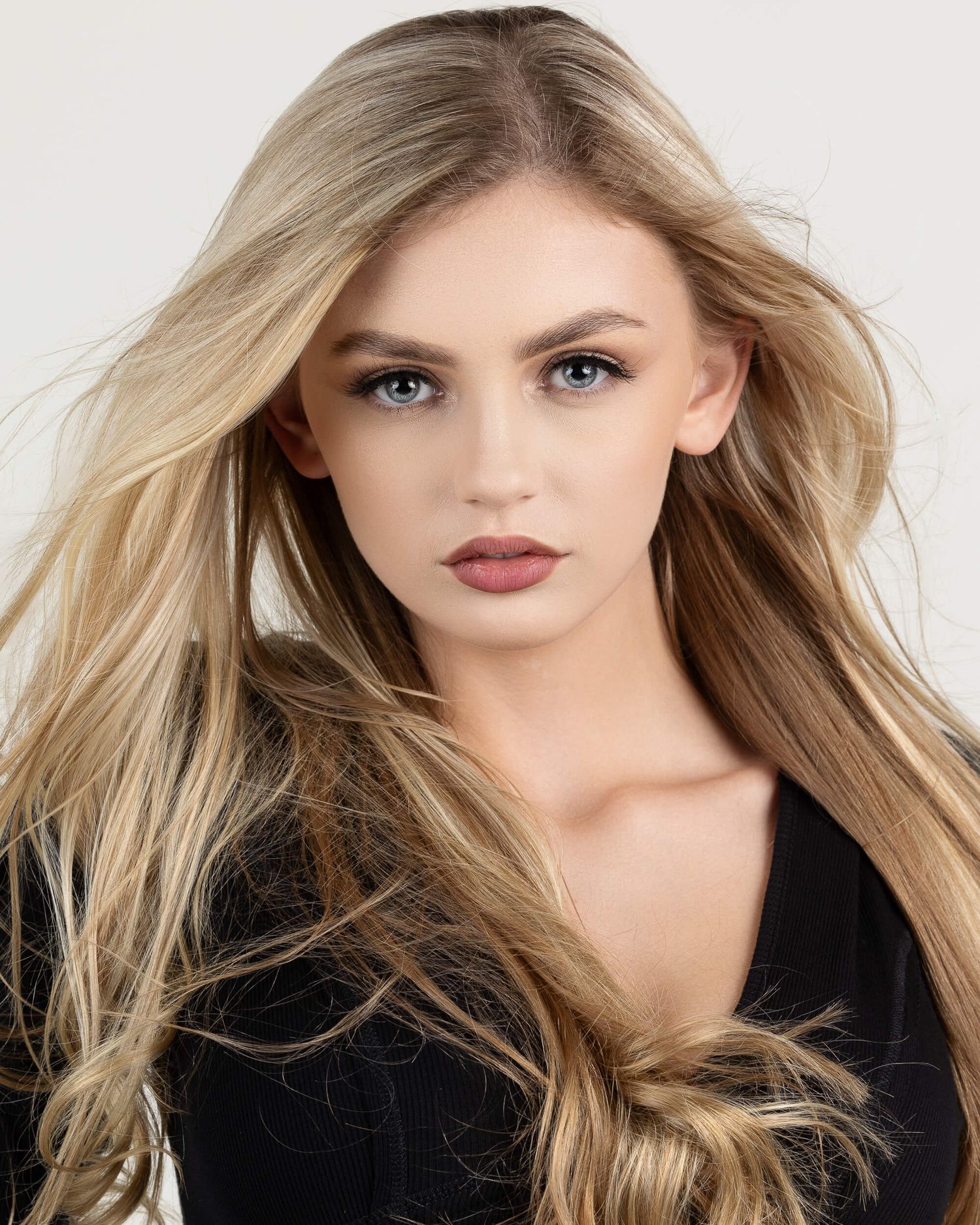 Blonde model with long wavy hair wearing black top against white background.