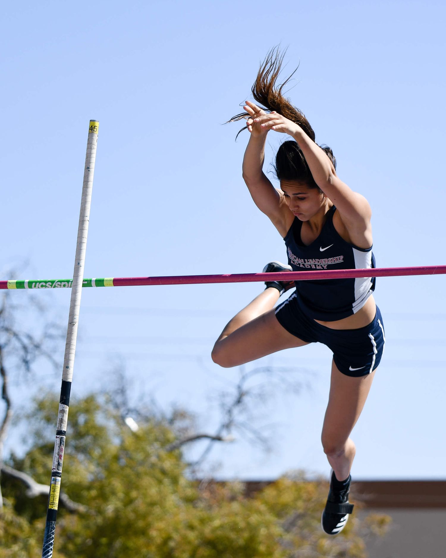 Female athlete clears bar during pole vault competition at outdoor track and field meet.