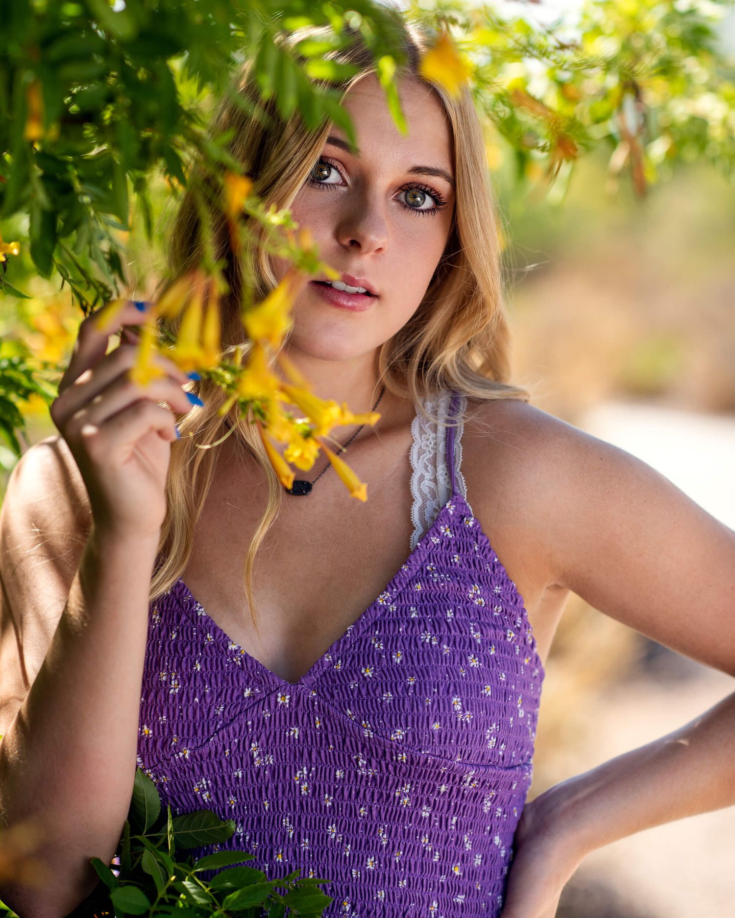 Blonde woman in purple floral top holding yellow flowers outdoors.