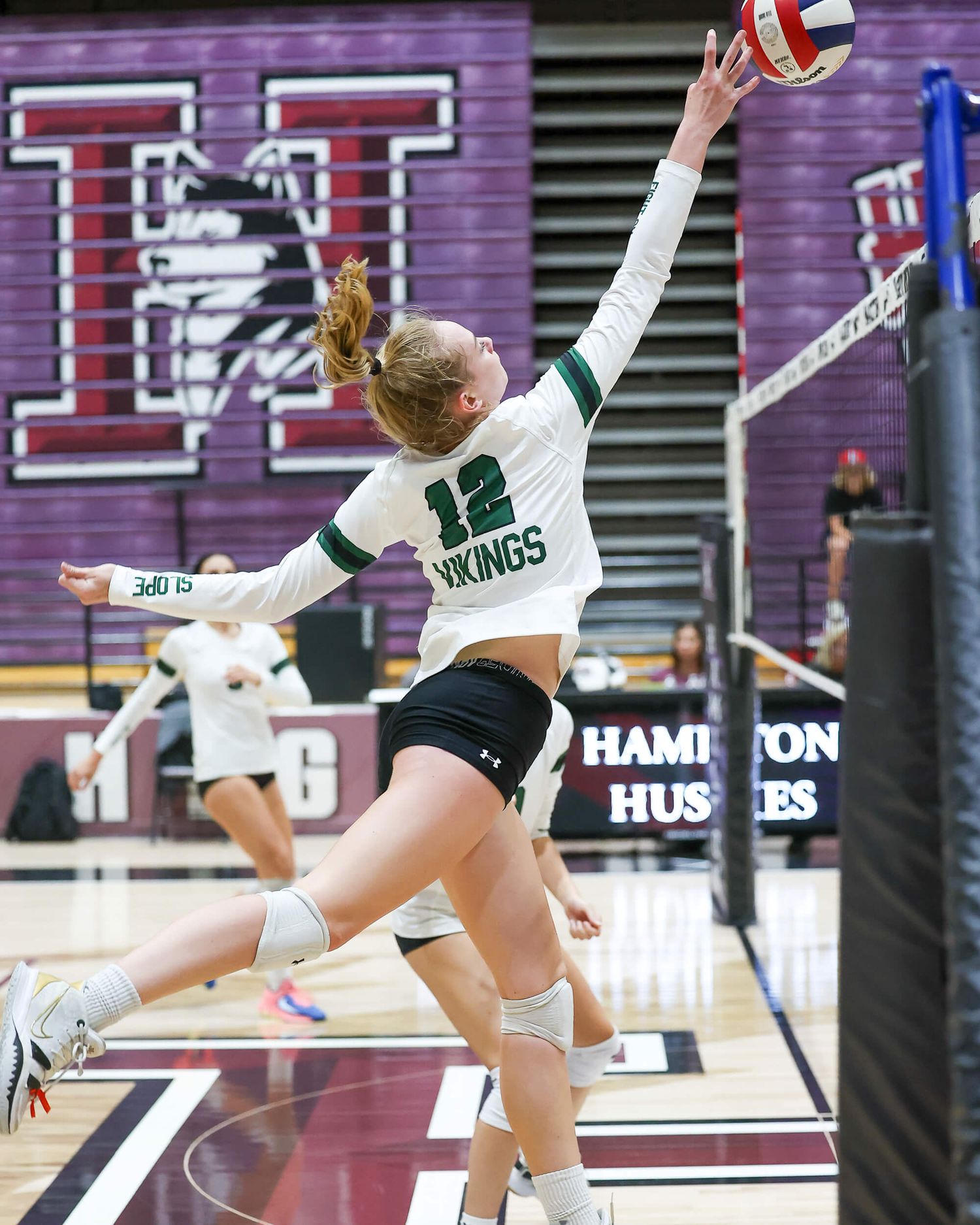 Vikings volleyball player number 12 reaches to tip the ball during an indoor gymnasium match.