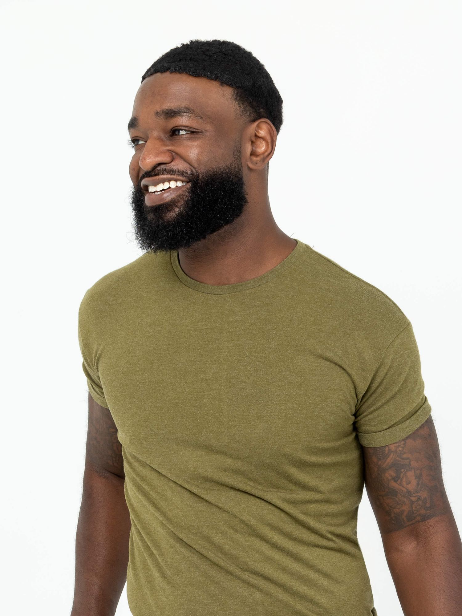 Smiling Black man with beard wearing olive green t-shirt against white background.