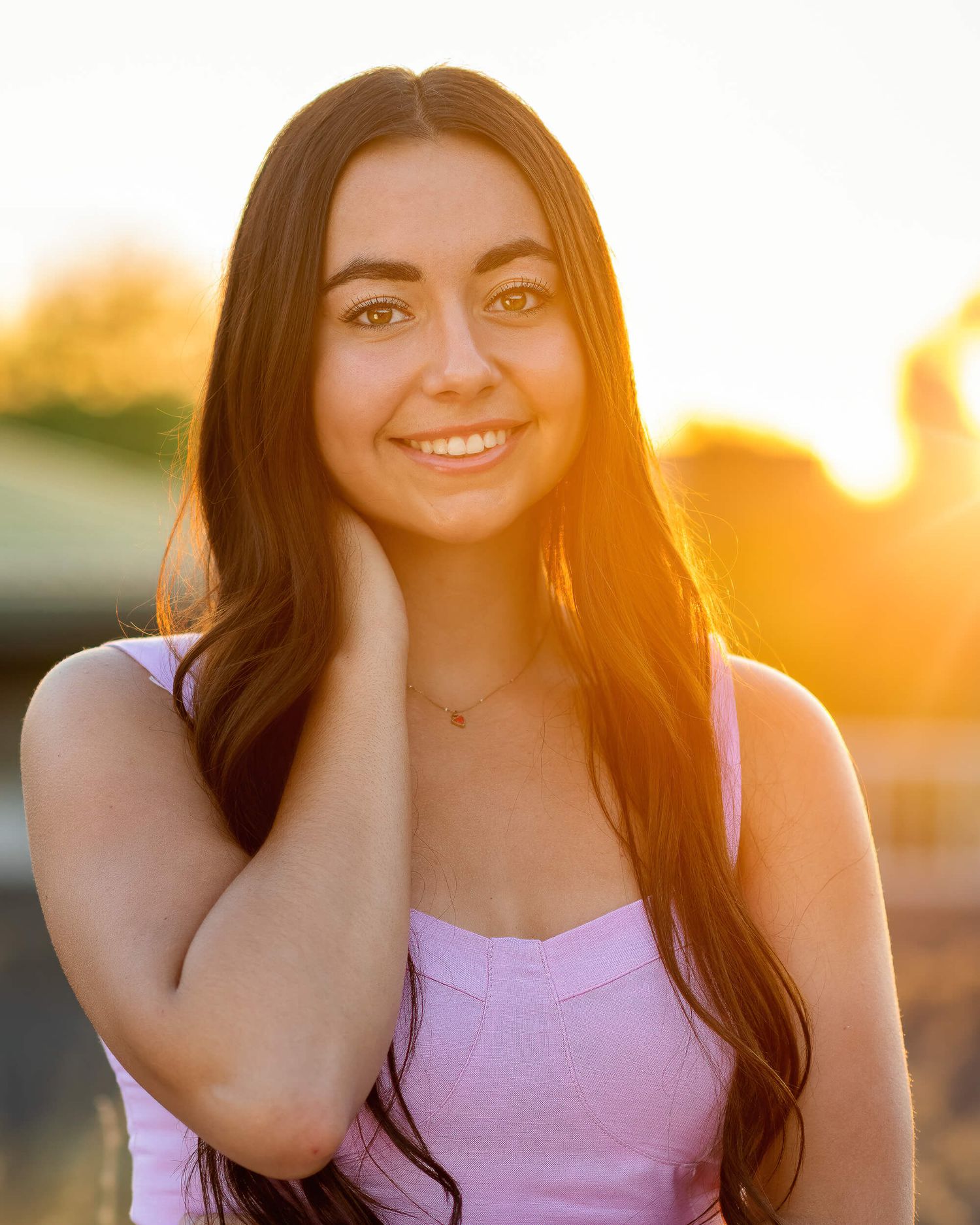 Smiling young woman in pink top with golden sunset backlight.