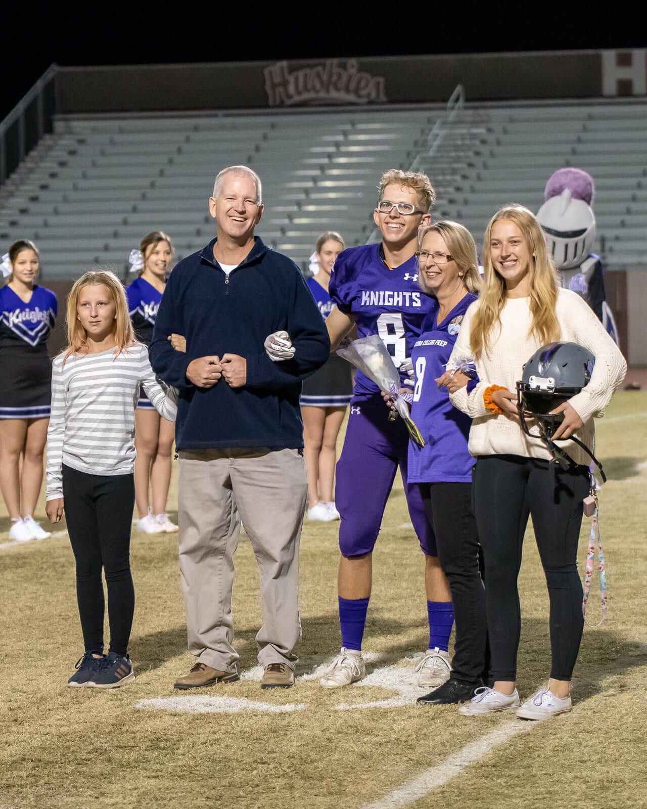 Family group poses together on a football field at night during a sports recognition ceremony.