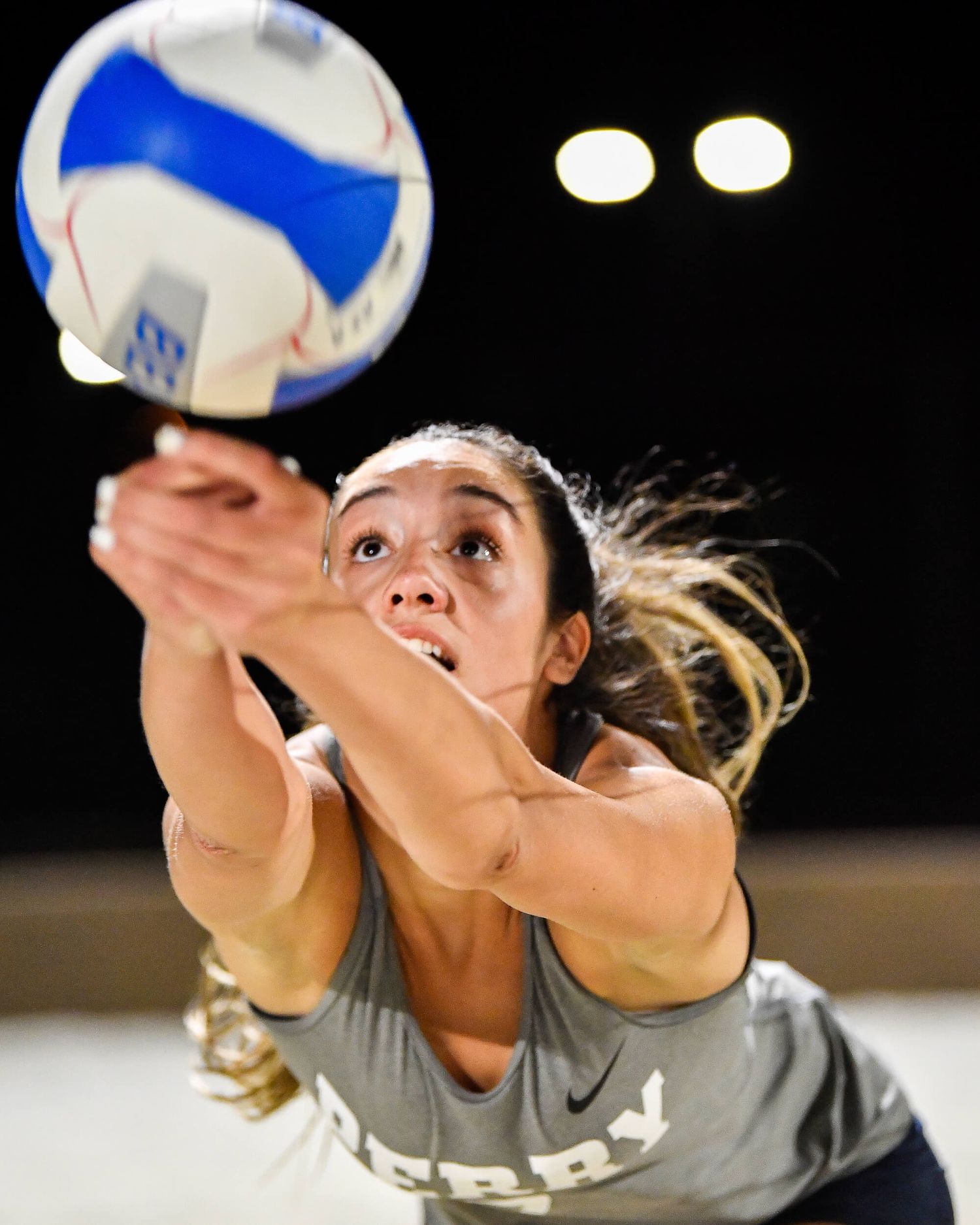 Female volleyball player digs the ball with focused intensity in a dramatic close-up action shot.