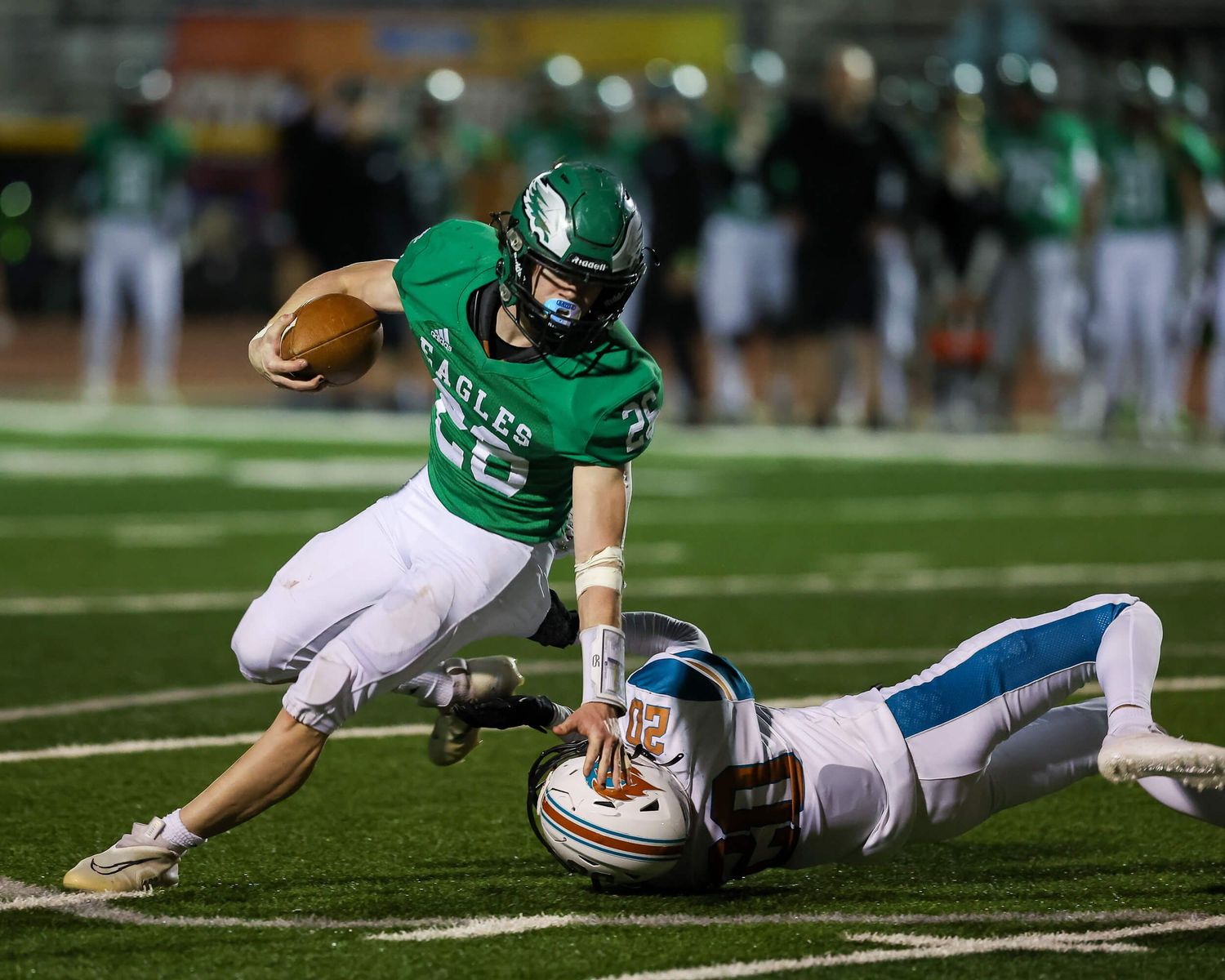 Eagles football player in green uniform evades a diving tackle during a night game on a lit field.