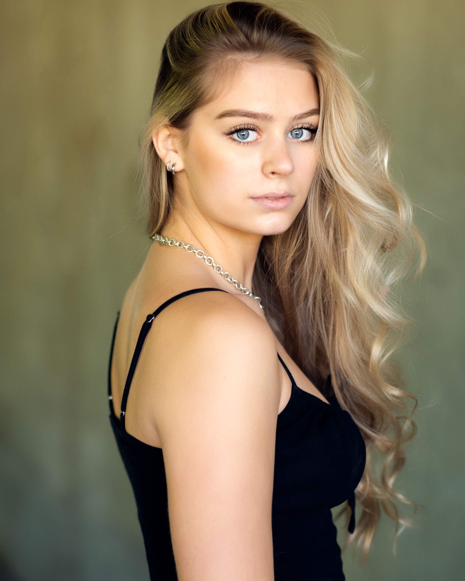 Blonde woman with blue eyes in black dress looking over shoulder with wavy hair.