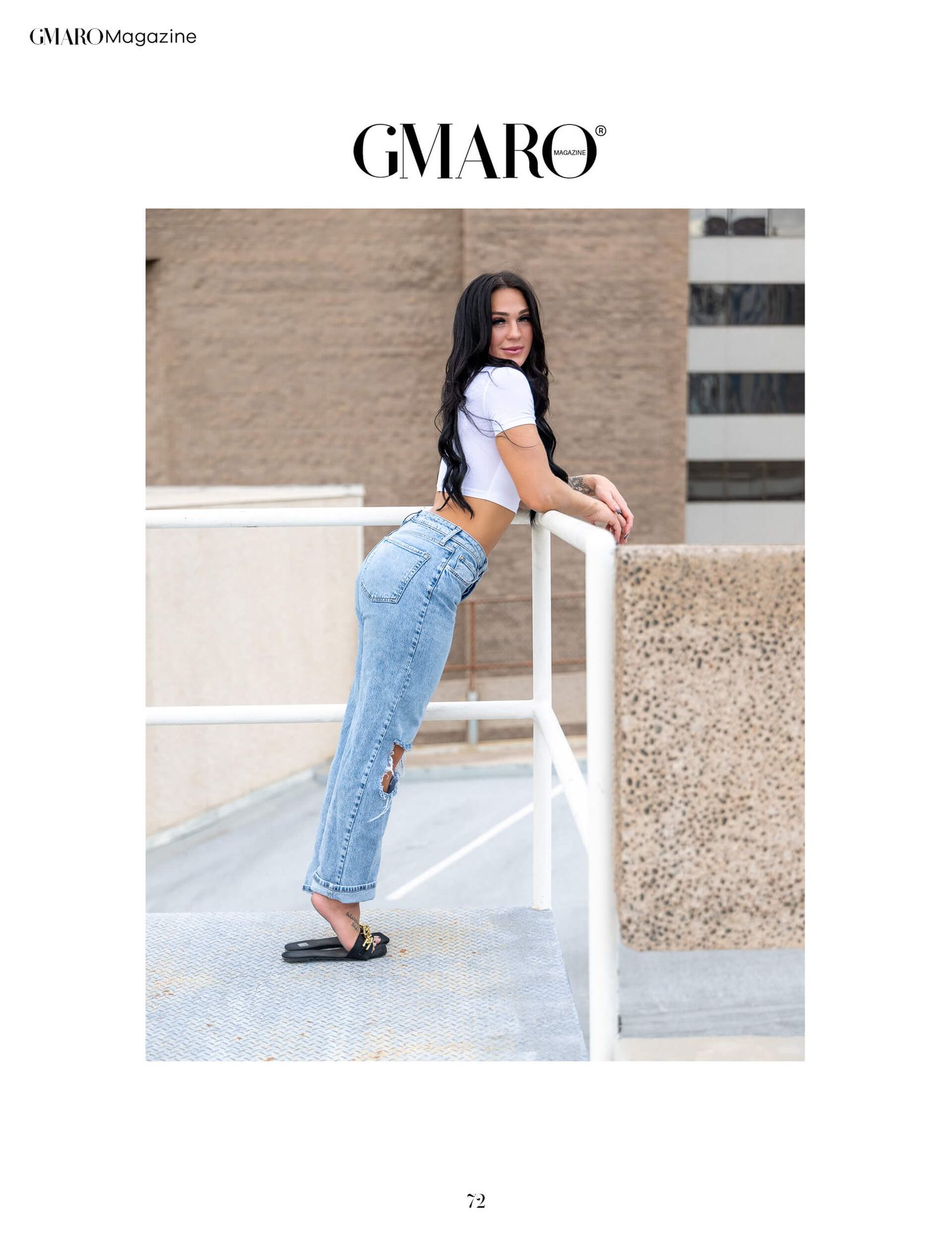 Woman in white crop top and light wash jeans leaning on railing outdoors.