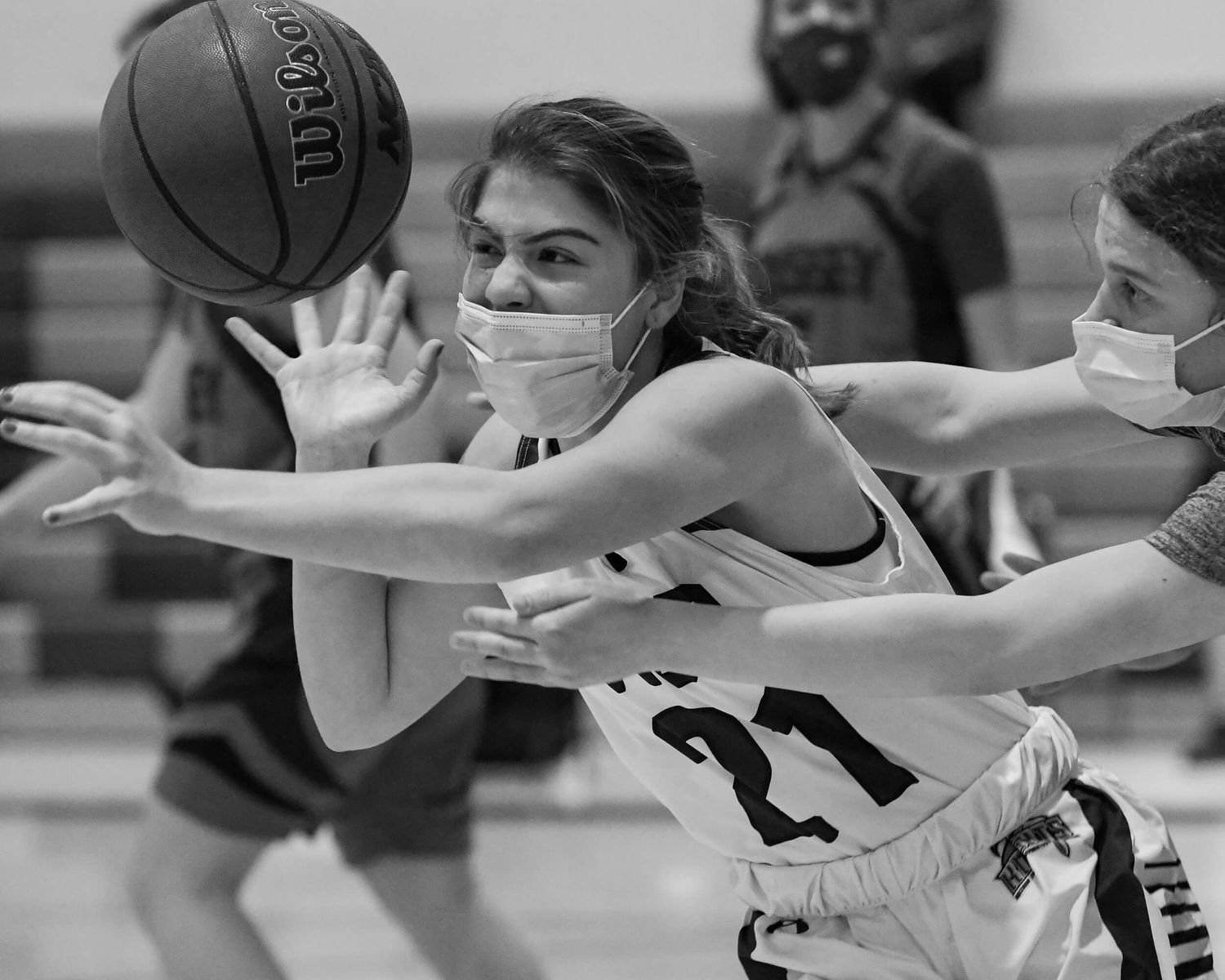 Black and white photo of two masked female basketball players competing for the ball.