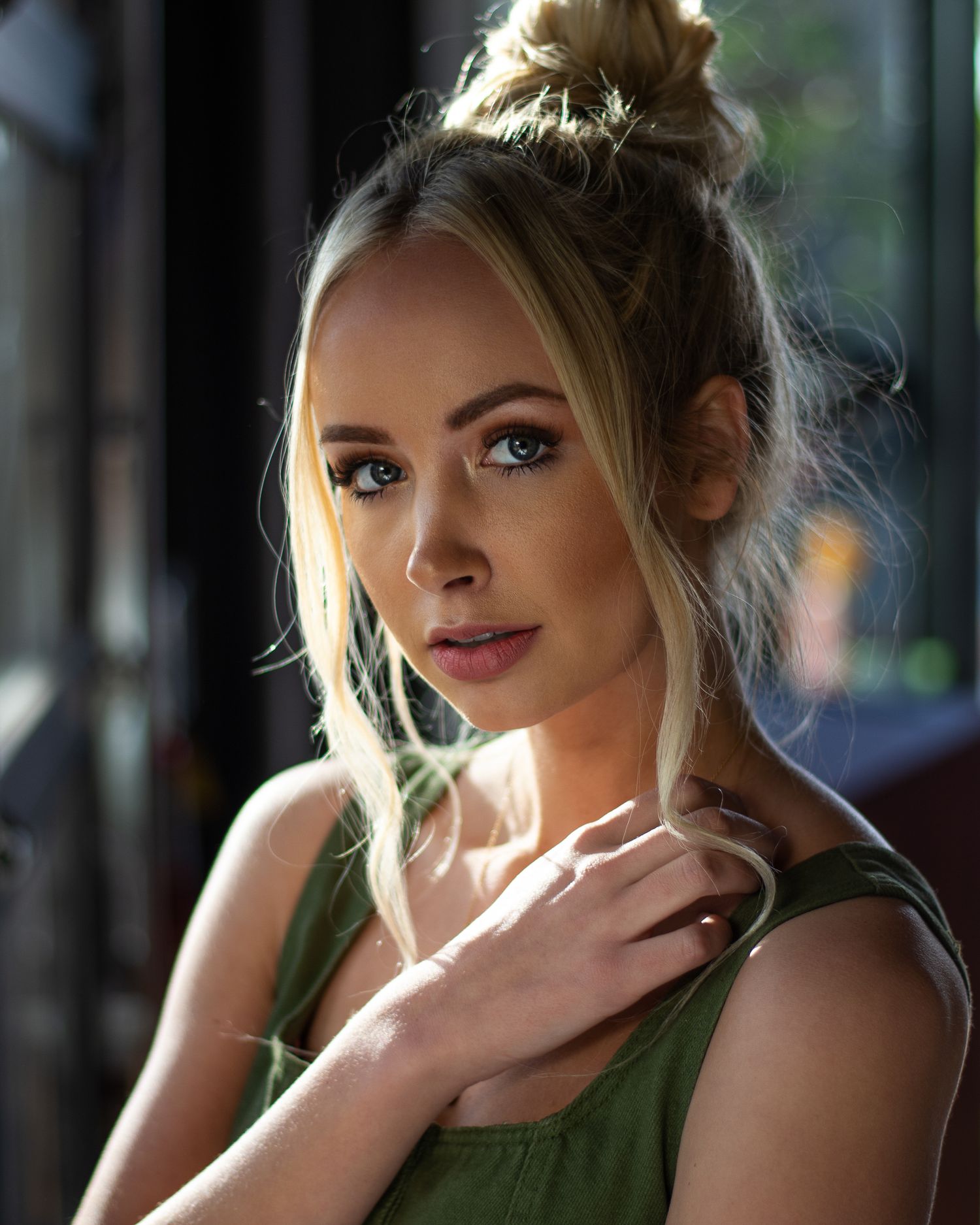 Beautiful blonde woman with blue eyes in green top with hair up in bun in natural light.
