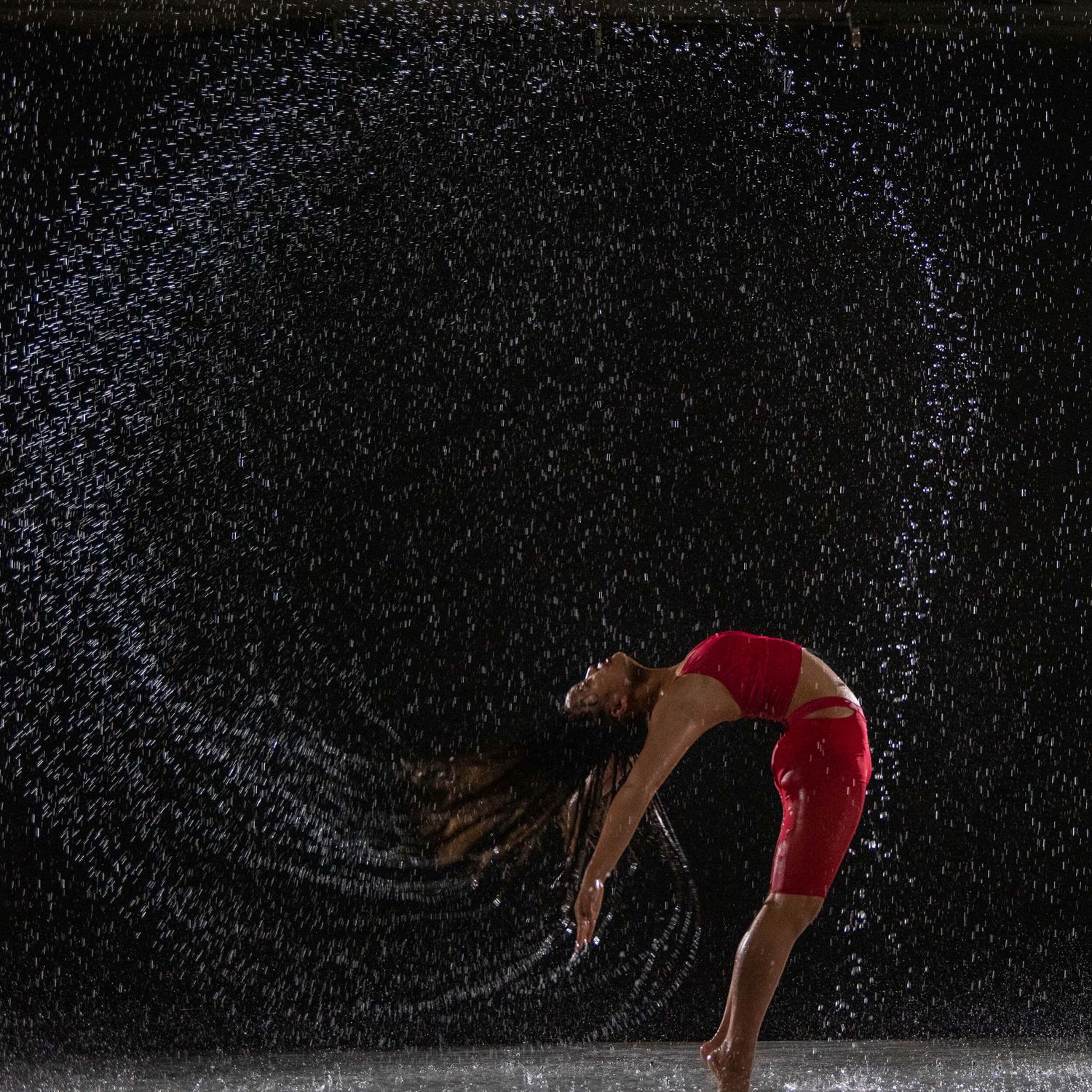 Dancer in red outfit performing backbend with water spray arc effect.
