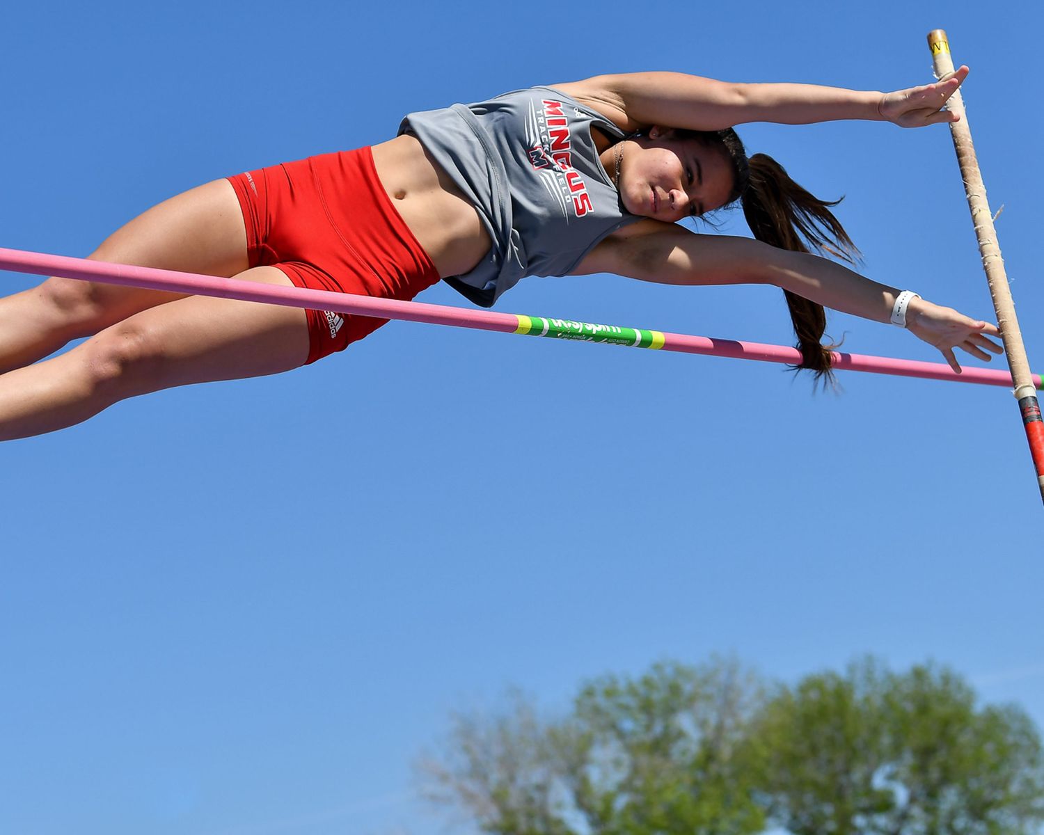 Female athlete performing pole vault, arching over the bar against a clear blue sky.