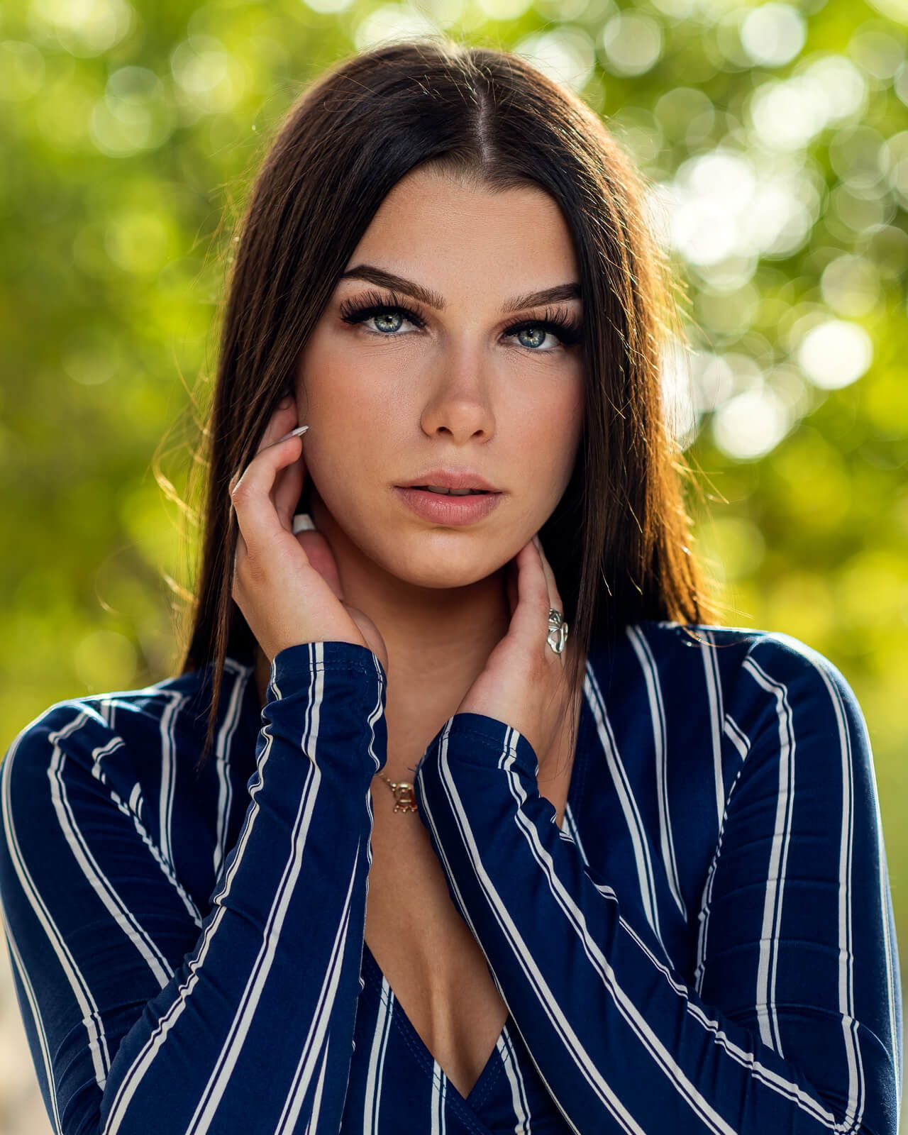 Beautiful brunette woman with blue eyes posing outdoors with bokeh background.