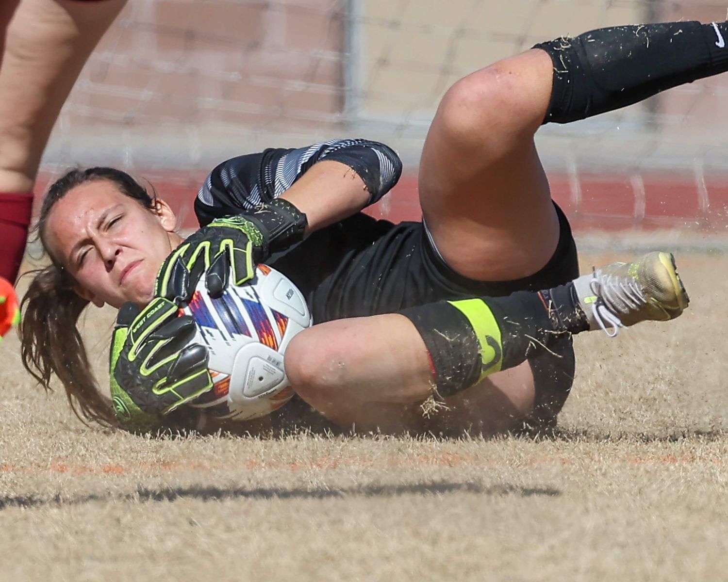 Female soccer goalkeeper dives to make save during muddy outdoor match.