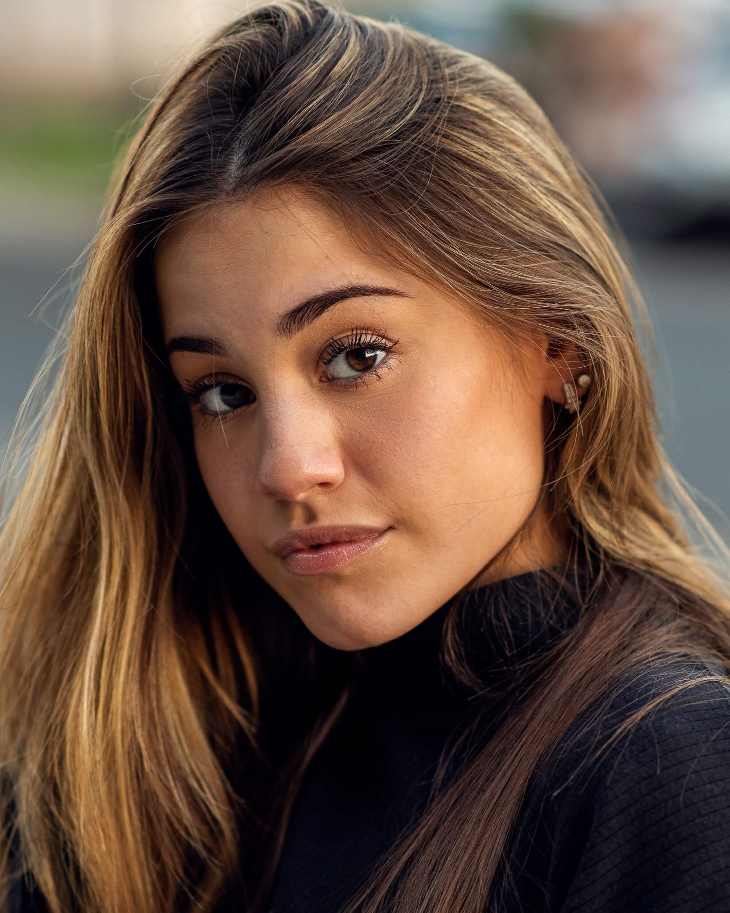 Young brunette woman with highlighted hair wearing black turtleneck in outdoor portrait.