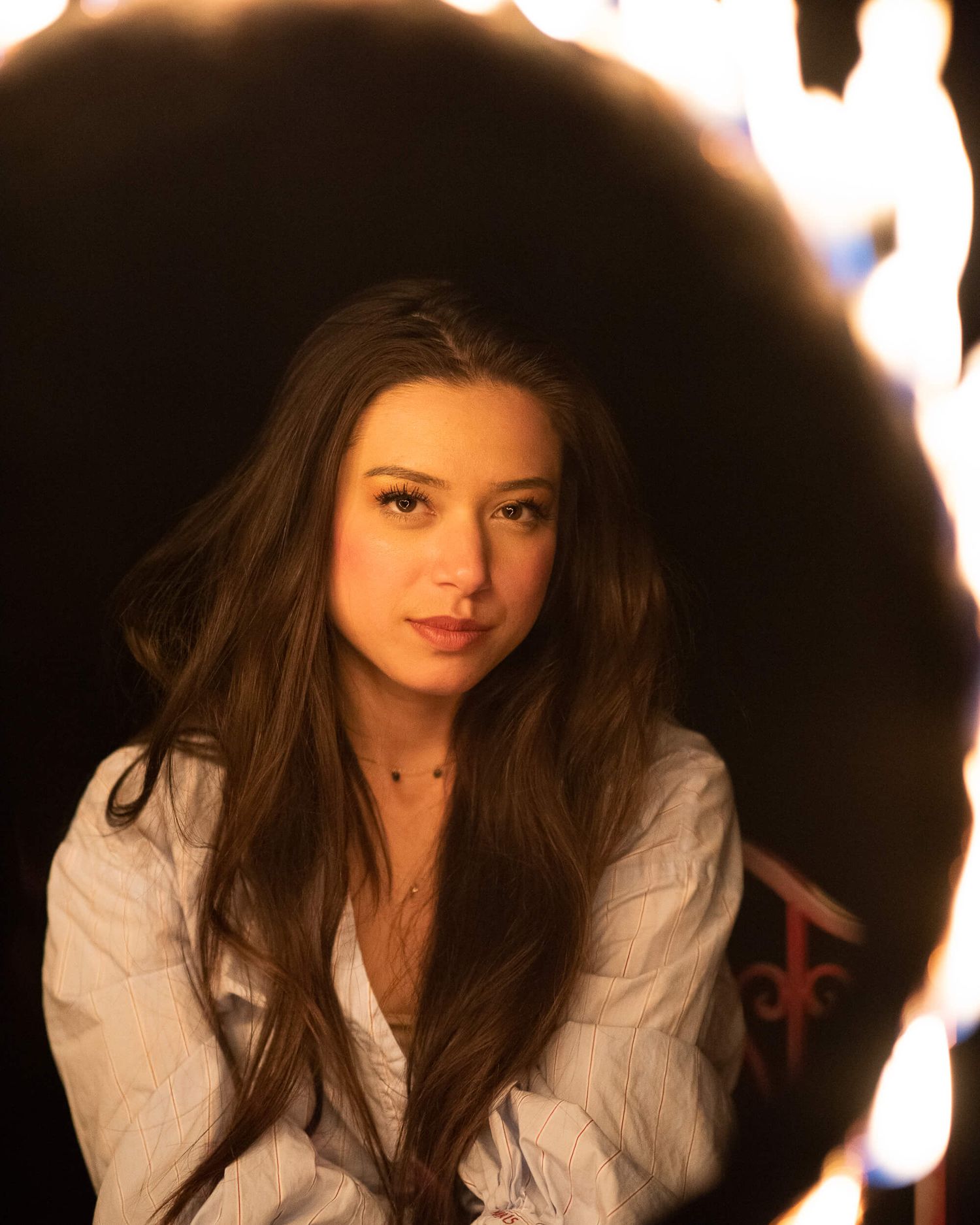 Young woman with long brown hair posing in white shirt surrounded by circular bokeh lights.