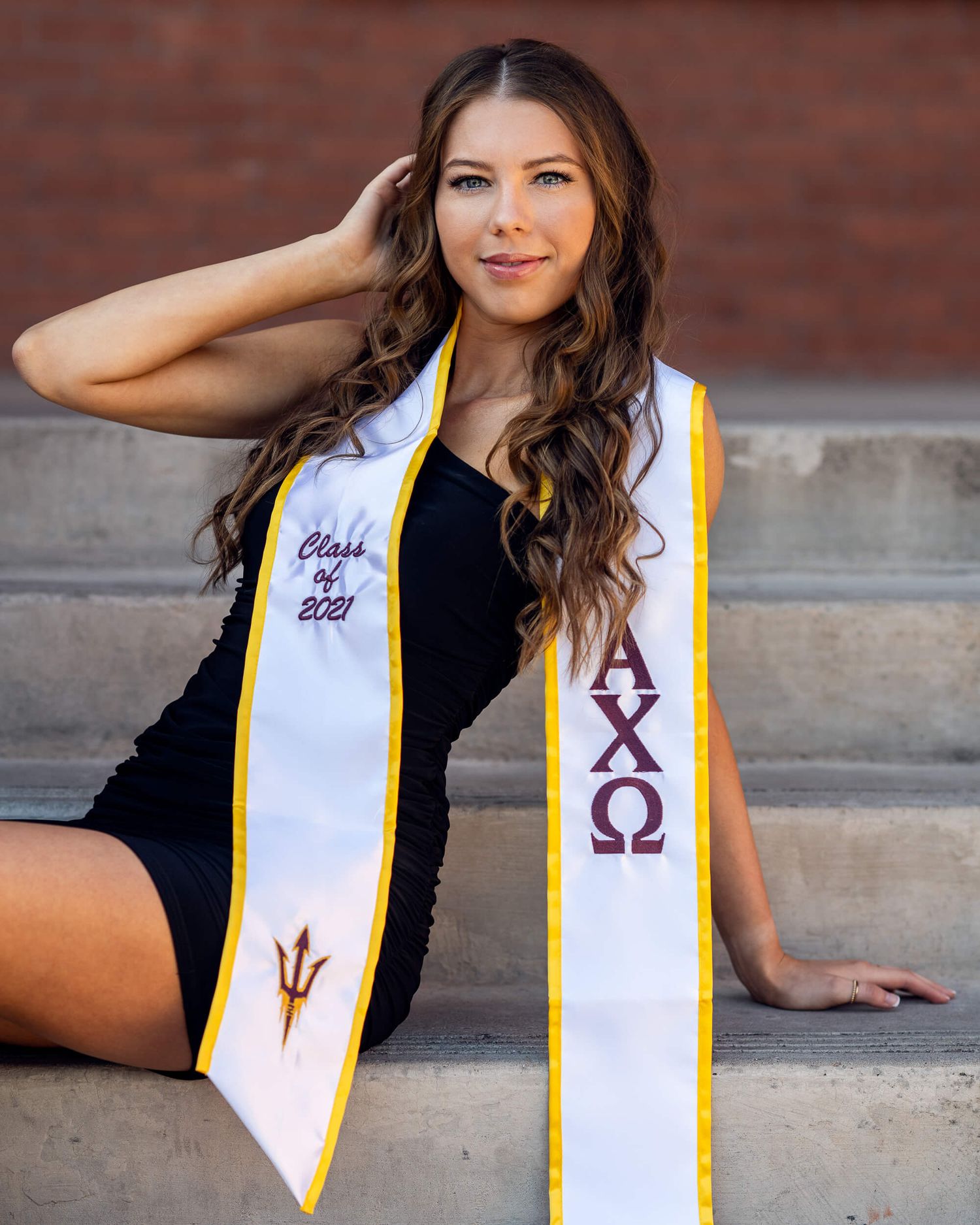 College graduate sitting on steps wearing Alpha Chi Omega stash and Class of 2021 graduation sash.