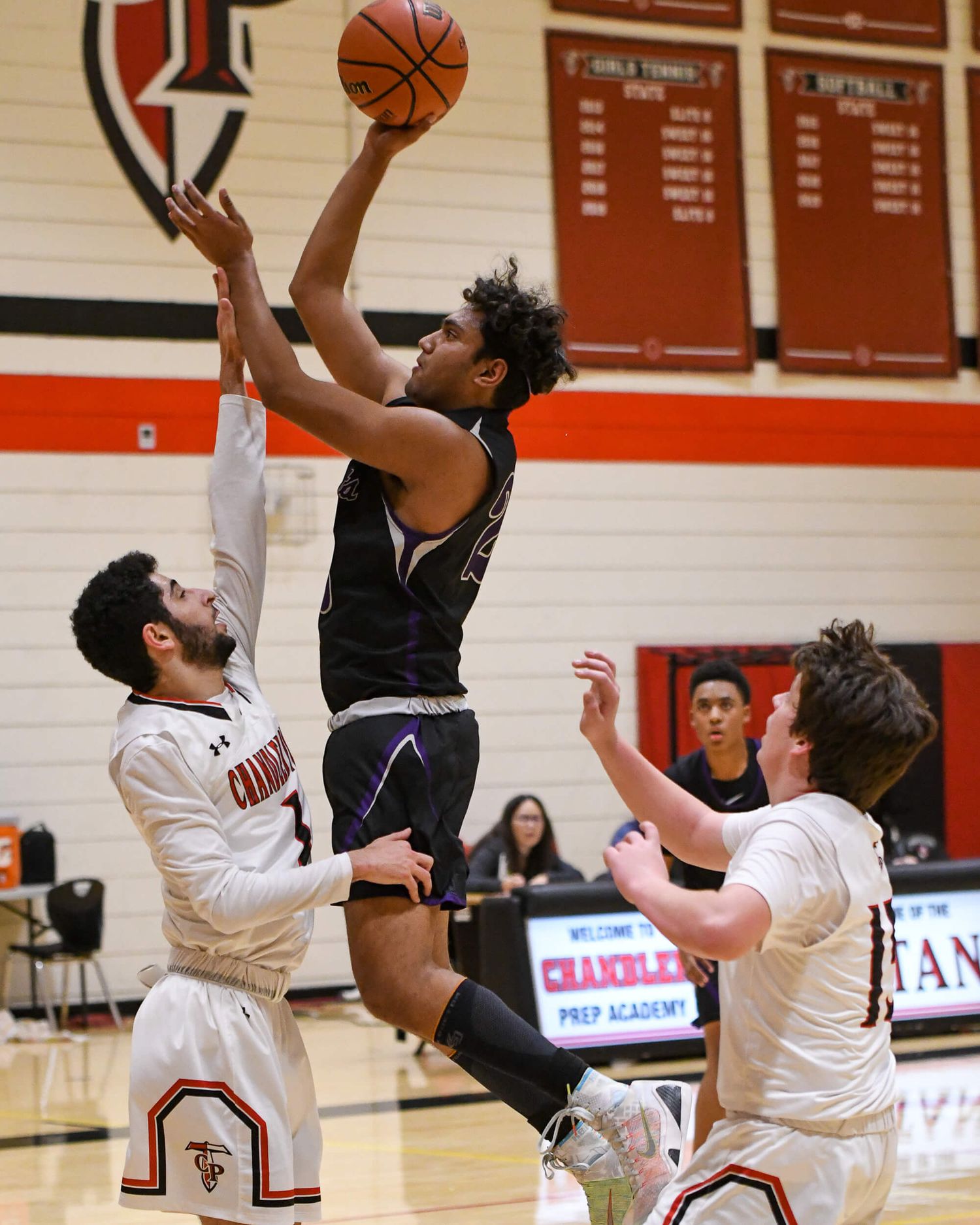 Basketball player in black uniform rises for a shot over two defenders in white.