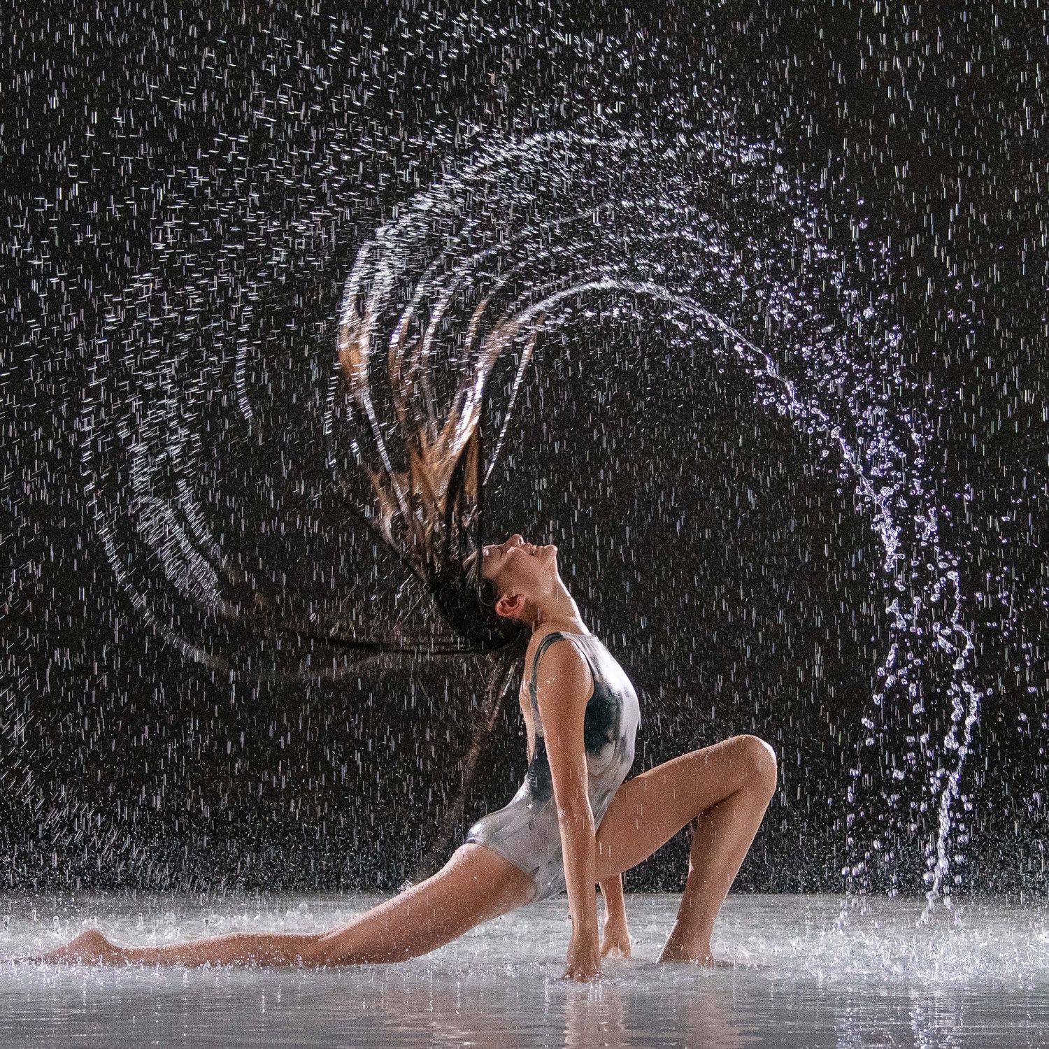 A dancer flips wet hair creating a stunning water arc splash against a dark background.