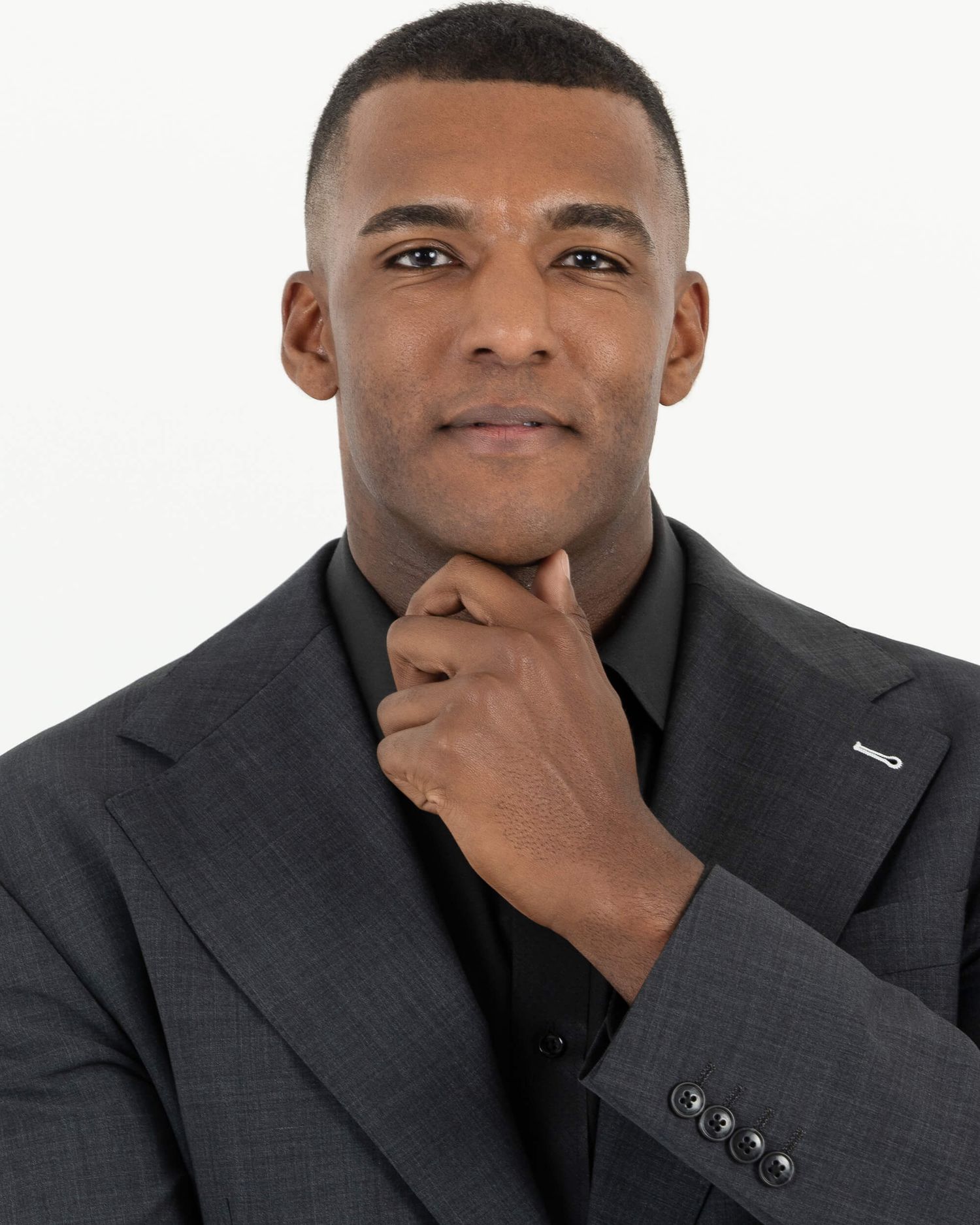 Professional man in dark suit posing thoughtfully with hand on chin against white background.