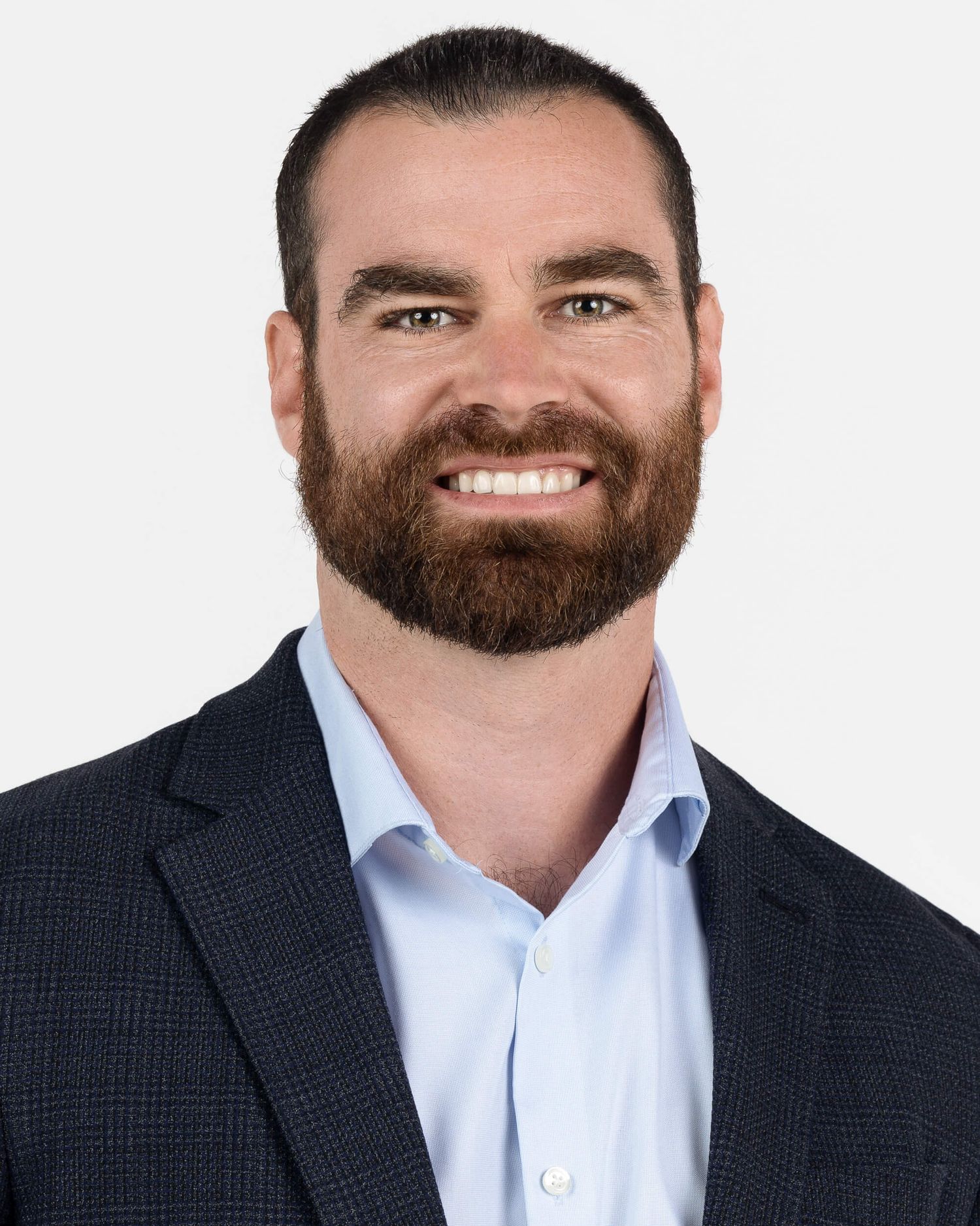 Professional headshot of a smiling bearded man wearing a light blue shirt and navy blazer against a white background.