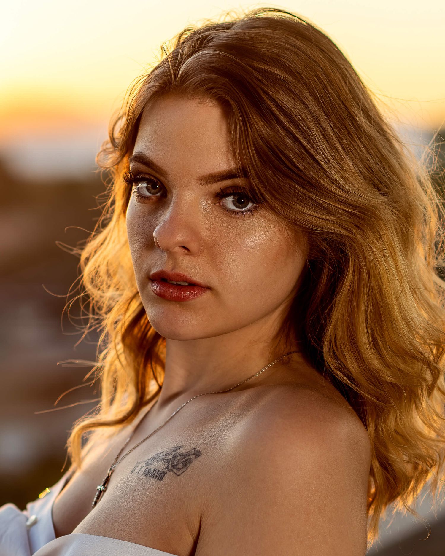 Young redhead woman with freckles and a tattoo poses at golden hour sunset outdoors.