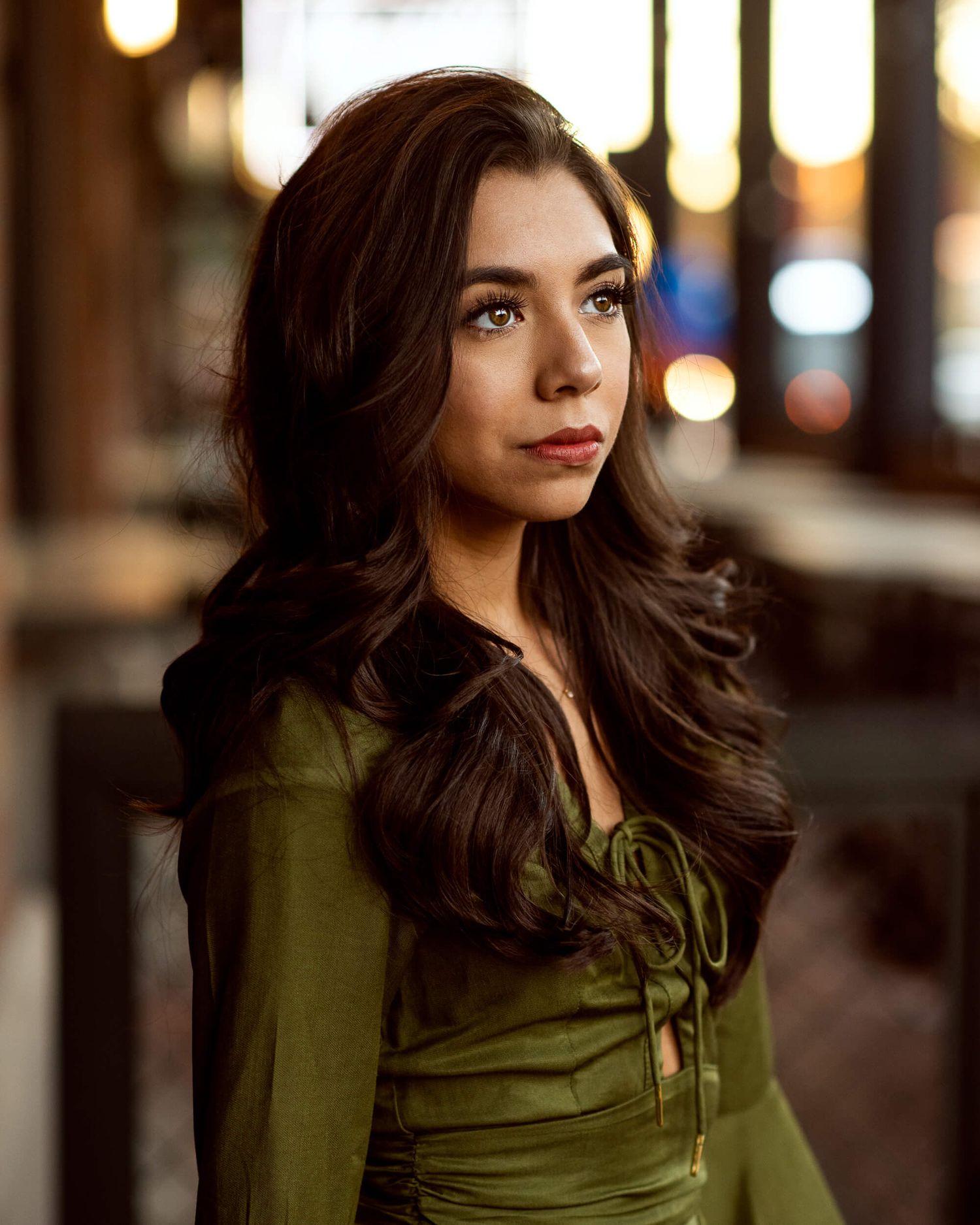 Young woman with dark hair in green dress under bokeh lights.