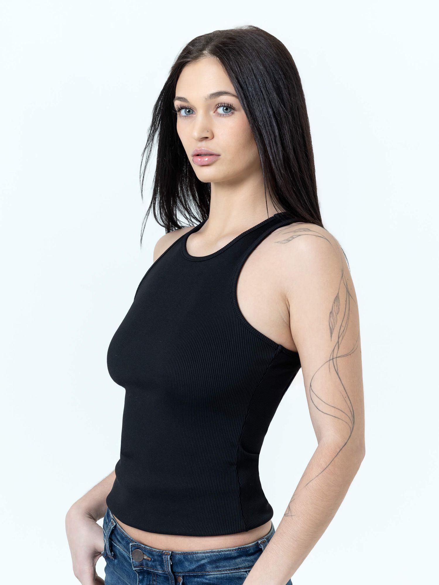 Woman wearing a black ribbed sleeveless crop top with jeans, featuring a racerback design and fitted silhouette.