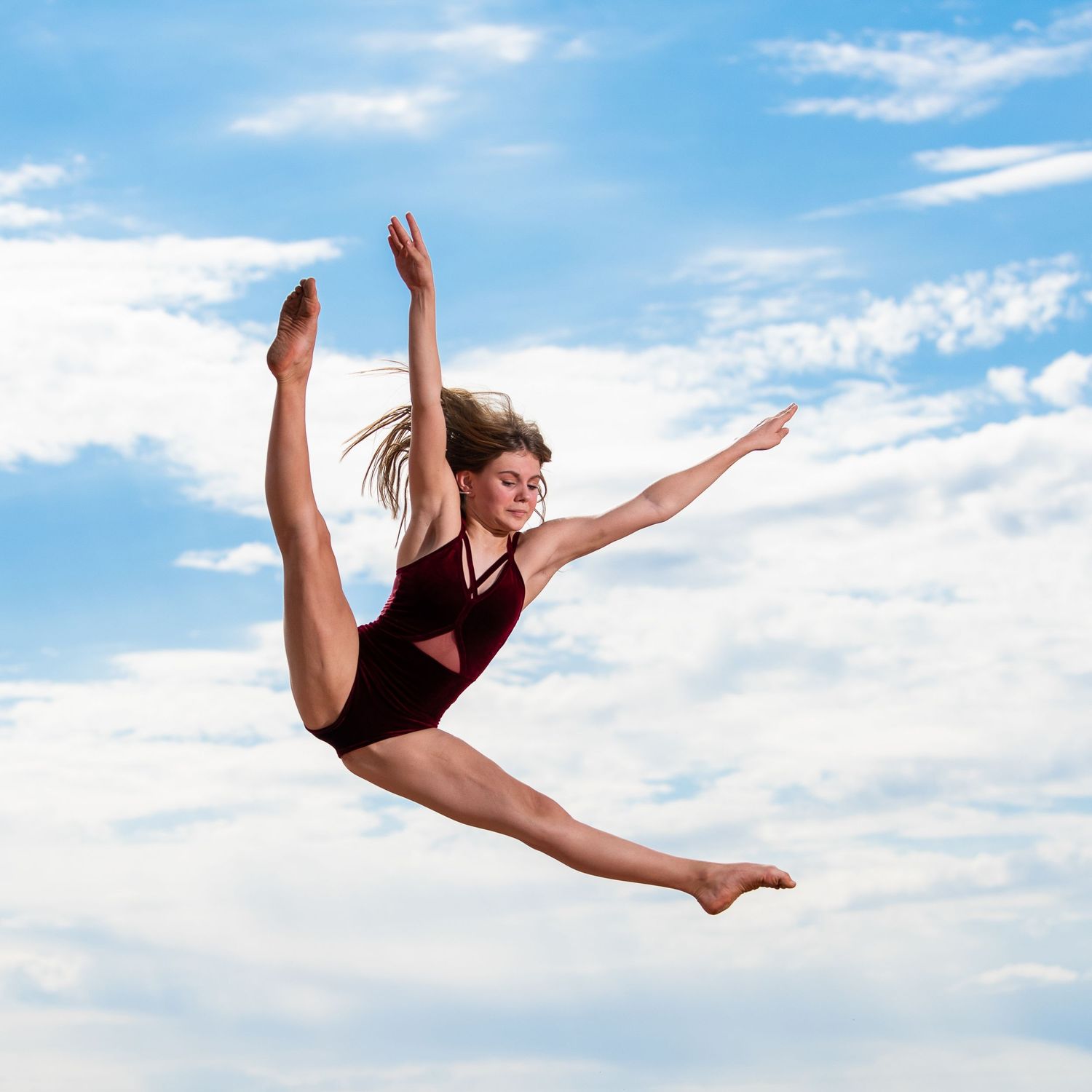 Athletic female dancer leaping gracefully against a blue sky background.