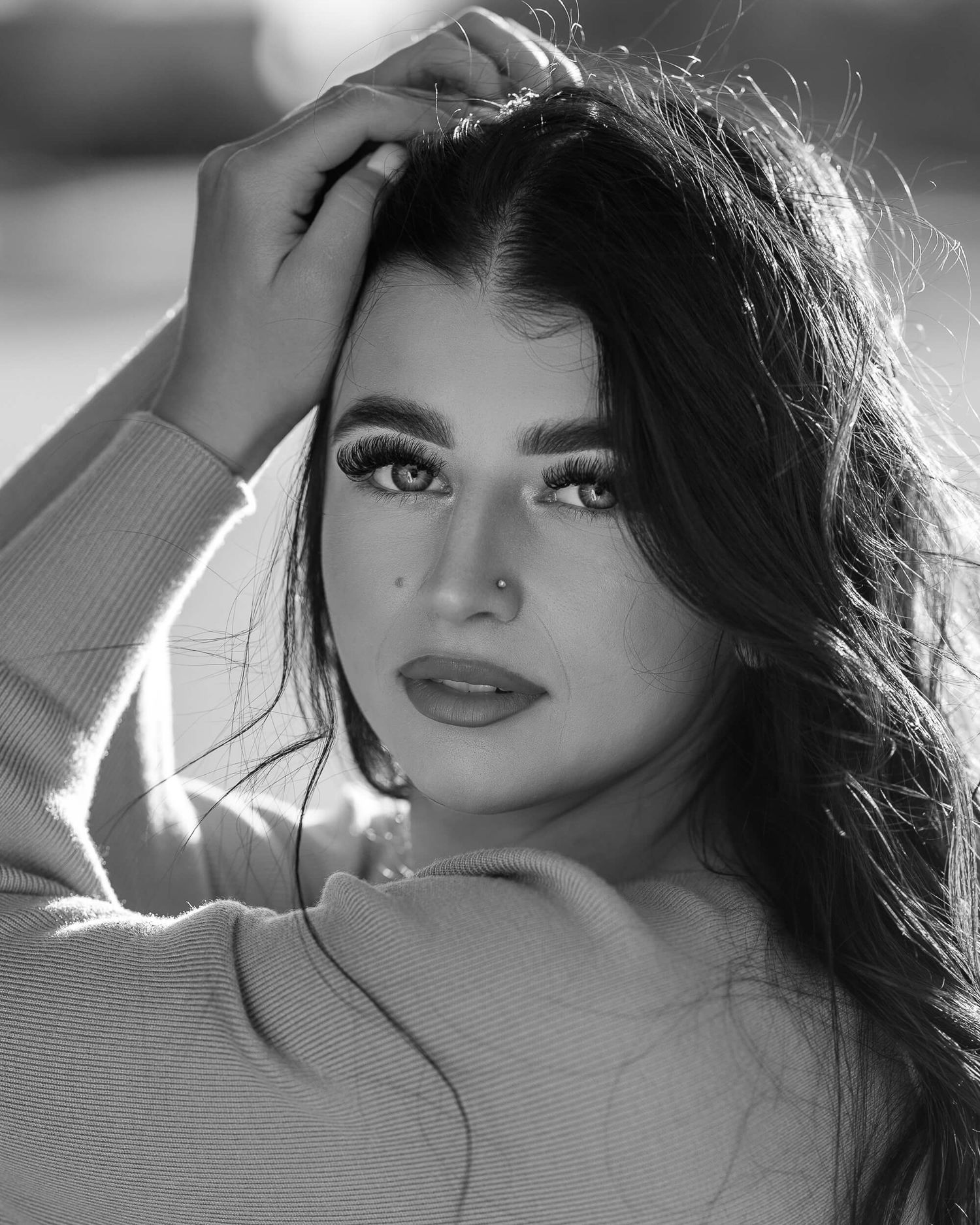 Black and white portrait of a young woman with dark hair and bold makeup in a soft sweater.