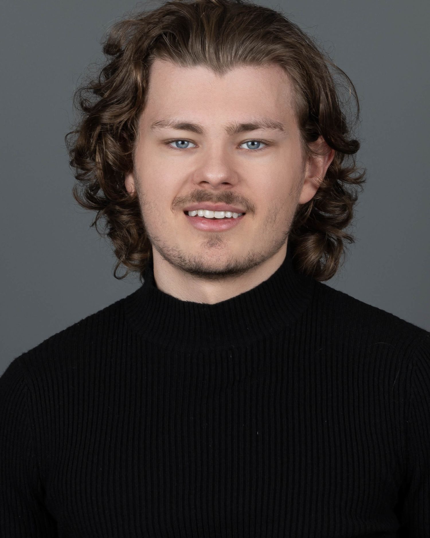 Young man with curly brown hair and blue eyes wearing black turtleneck sweater.