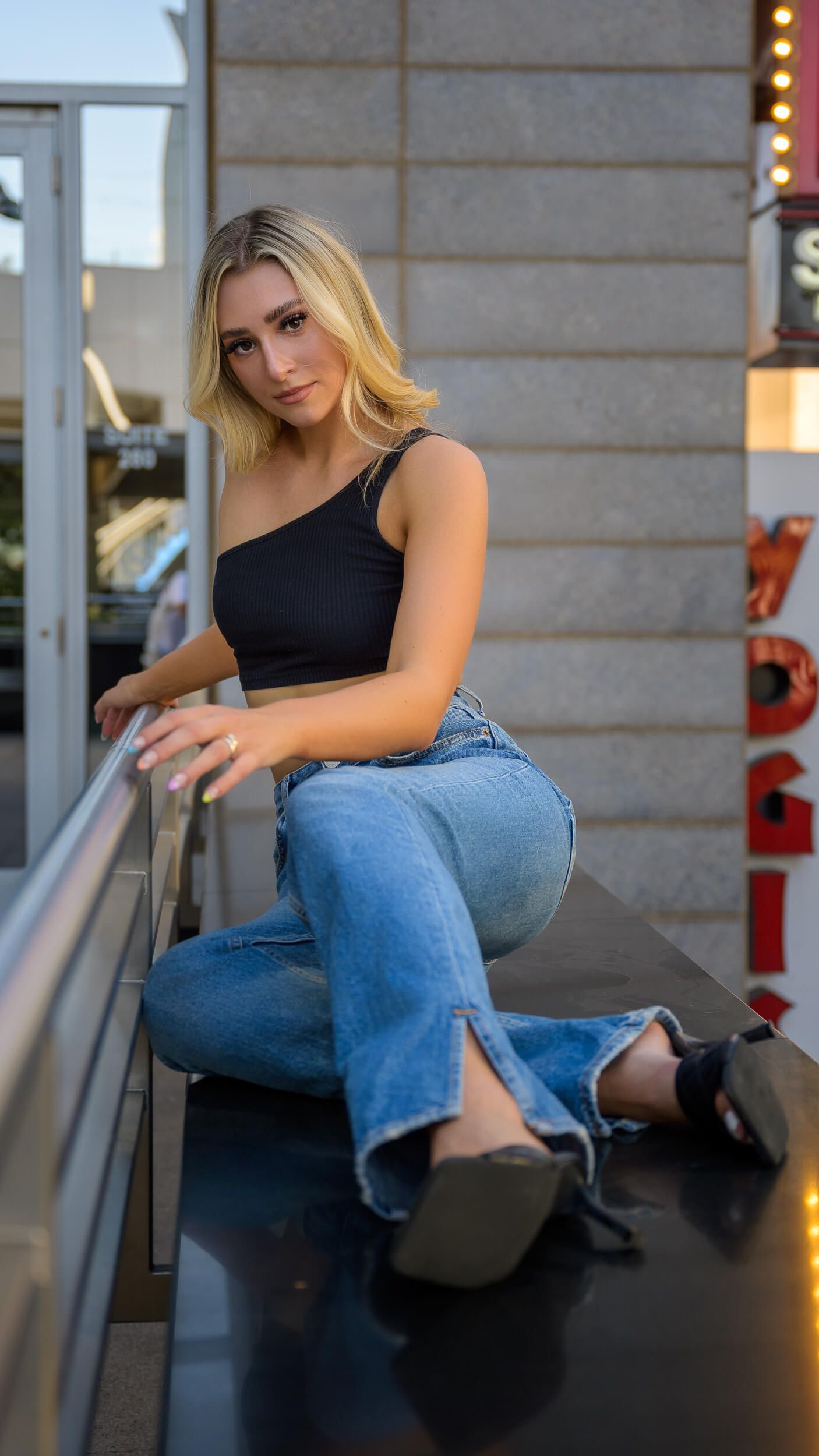 Blonde woman in black crop top and jeans posing on urban balcony.